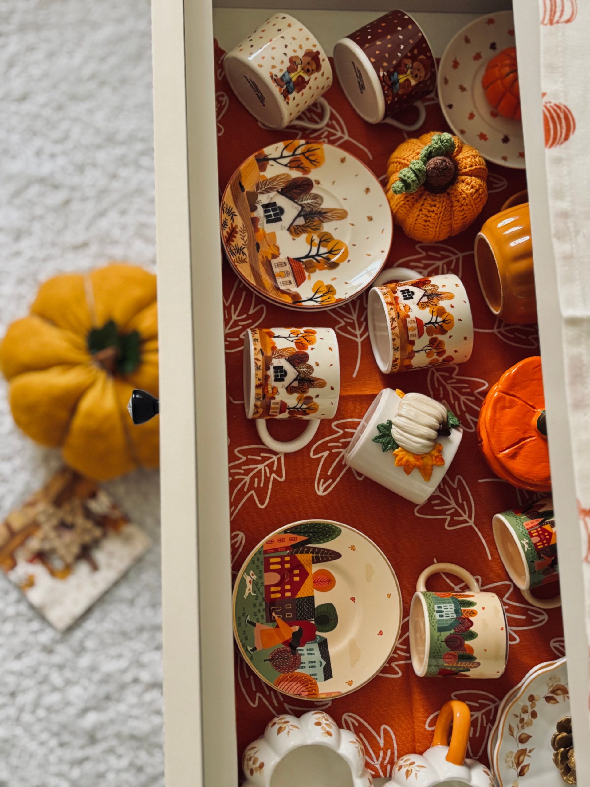 Charming autumn-themed crockery with pumpkins and fall designs neatly arranged in a drawer.