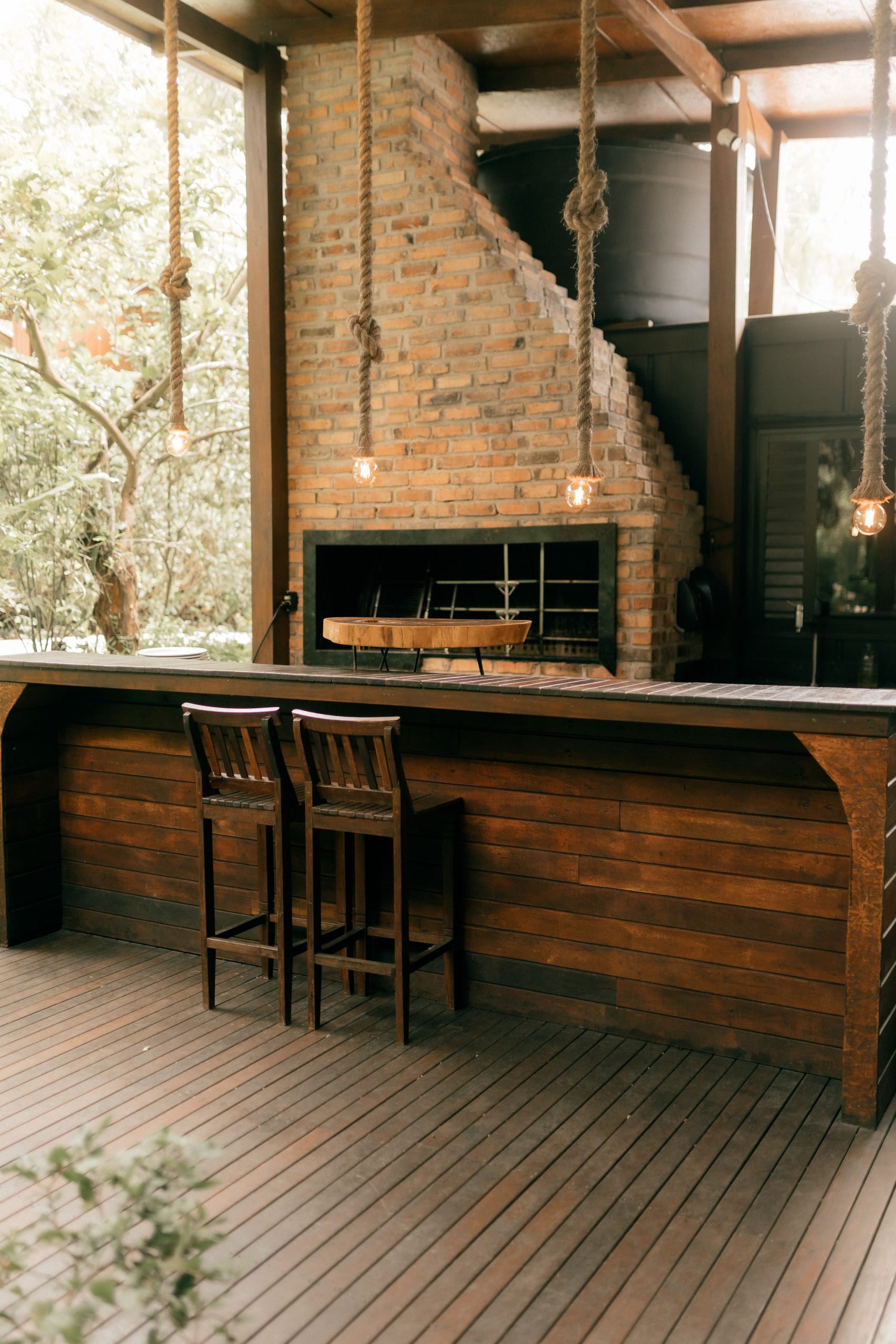 Charming outdoor seating area with rustic wooden bar and brick fireplace surrounded by nature.