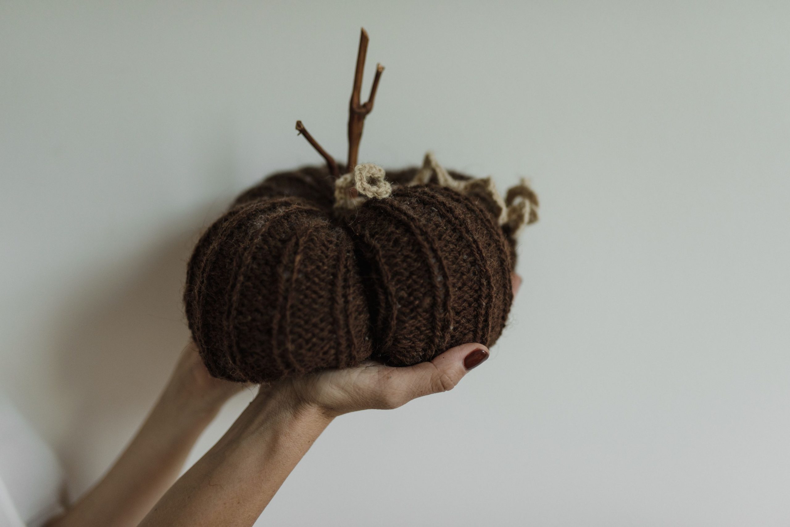Close-up of a knitted pumpkin craft held by hands against a light background.