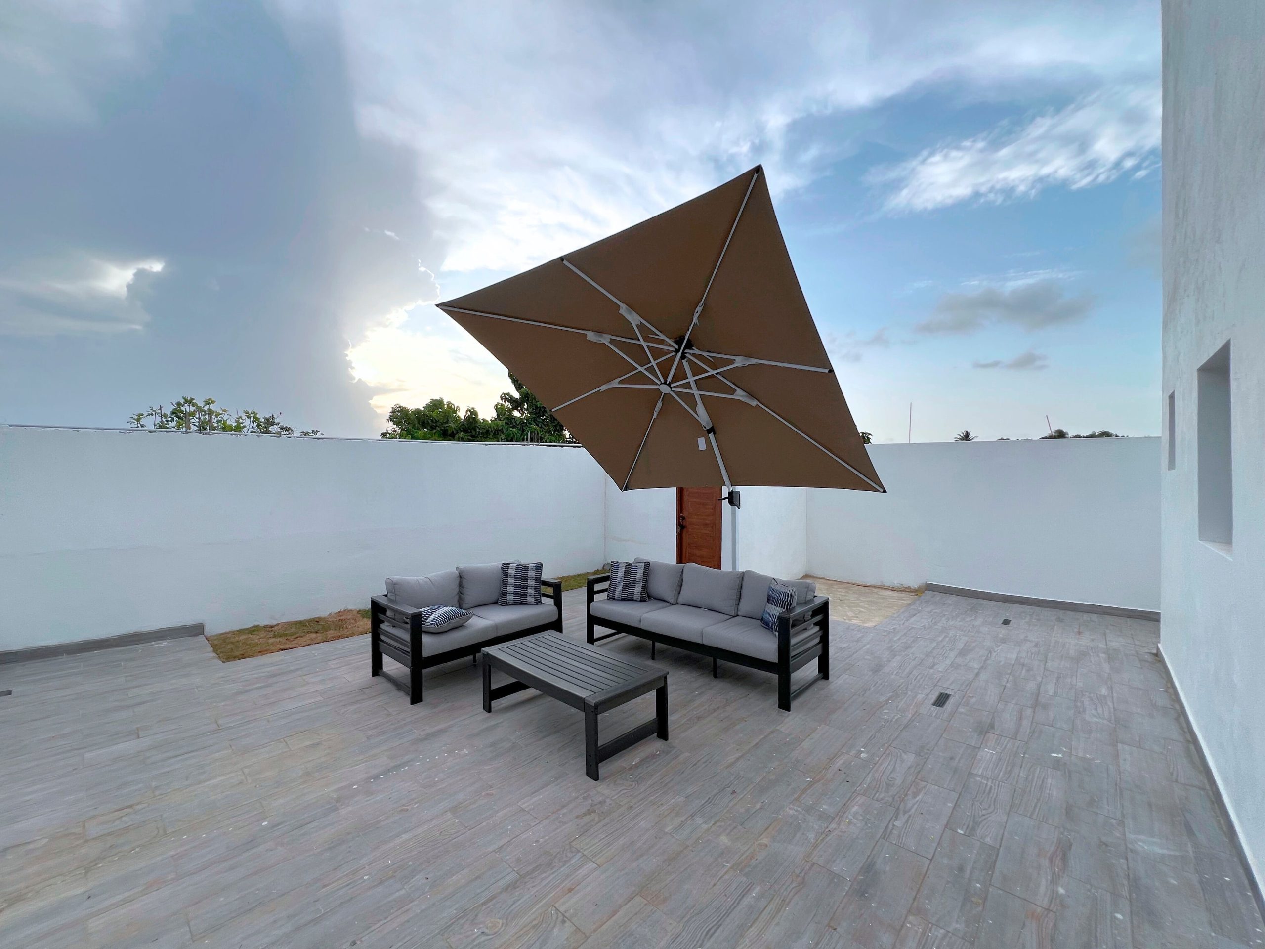 Contemporary outdoor patio featuring a sofa set and umbrella under a cloudy sky.