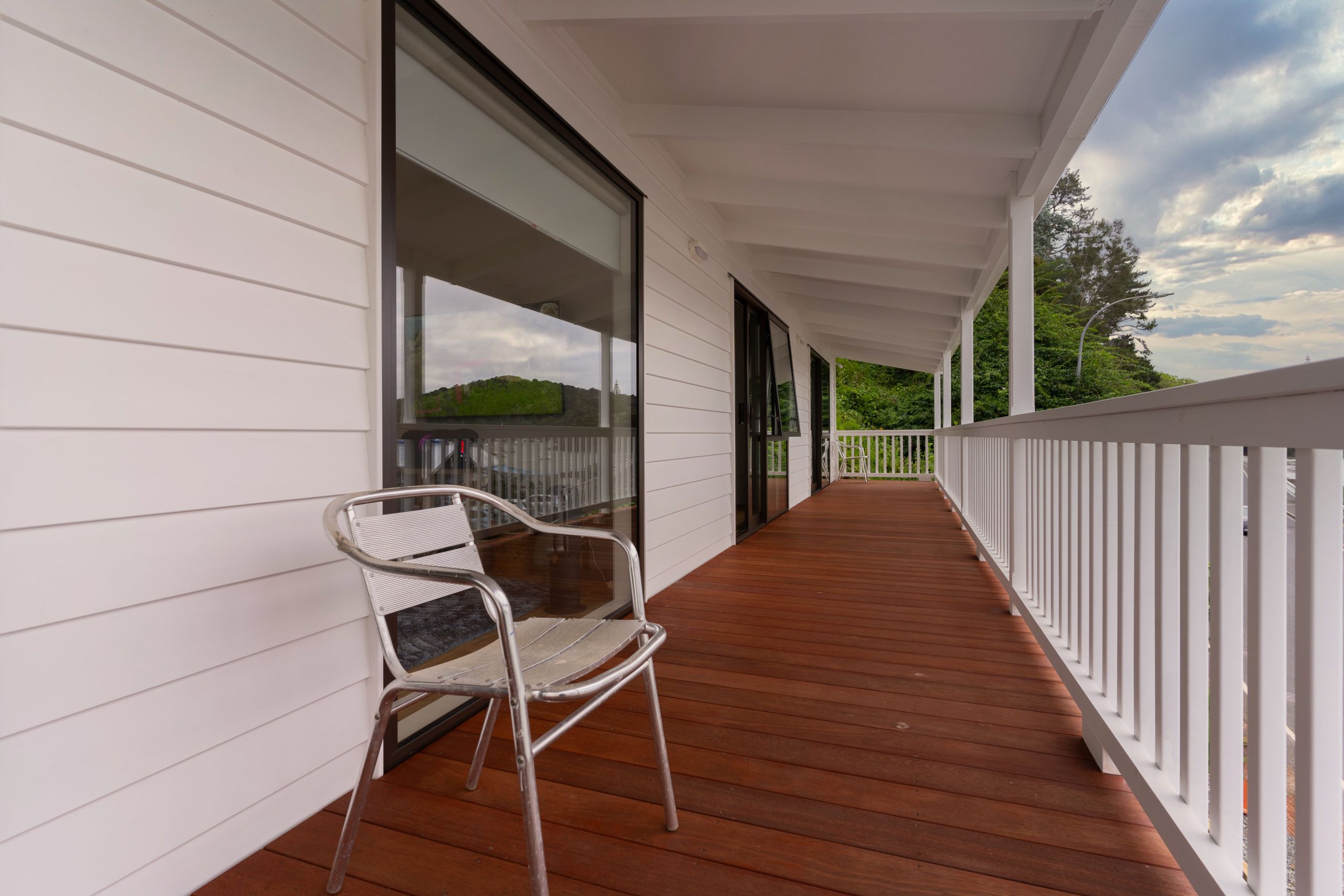 Contemporary wooden porch with metal chair, white facade, outdoor setting.