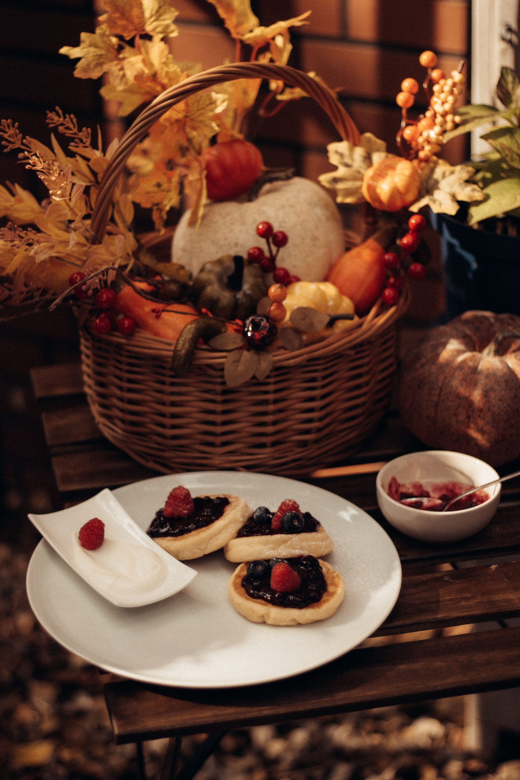 Cozy autumn setup with berry pastries and a harvest basket featuring pumpkins and leaves.