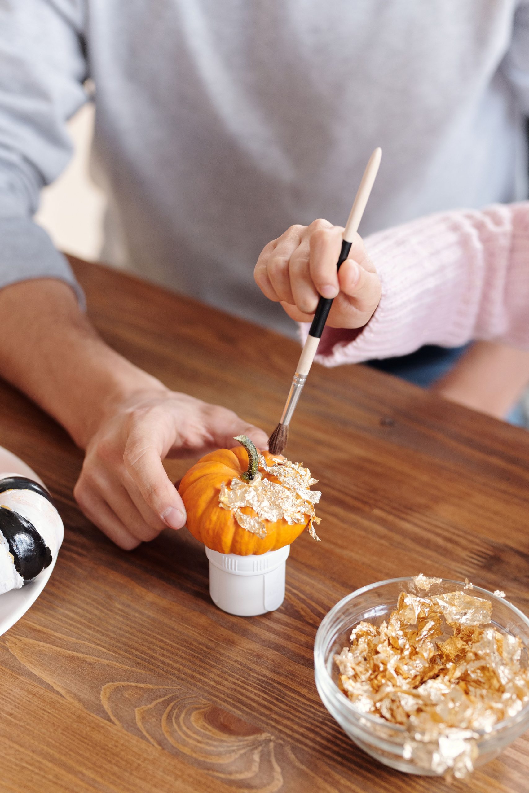 Creative Halloween activity with gold decorations on a small pumpkin by father and child indoors.