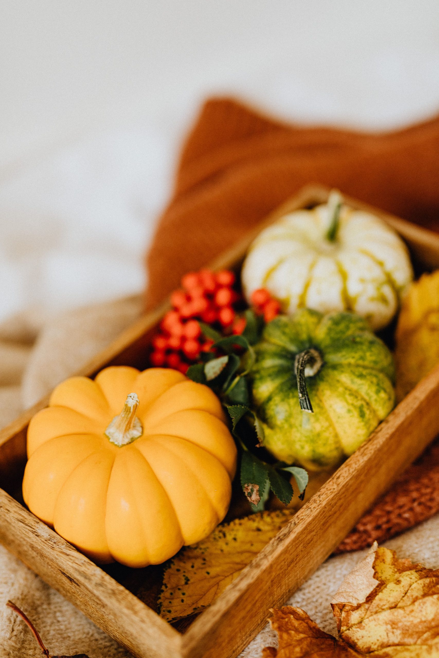 Elegant autumn harvest scene with mini pumpkins and leaves in a wooden tray, perfect for fall decor.
