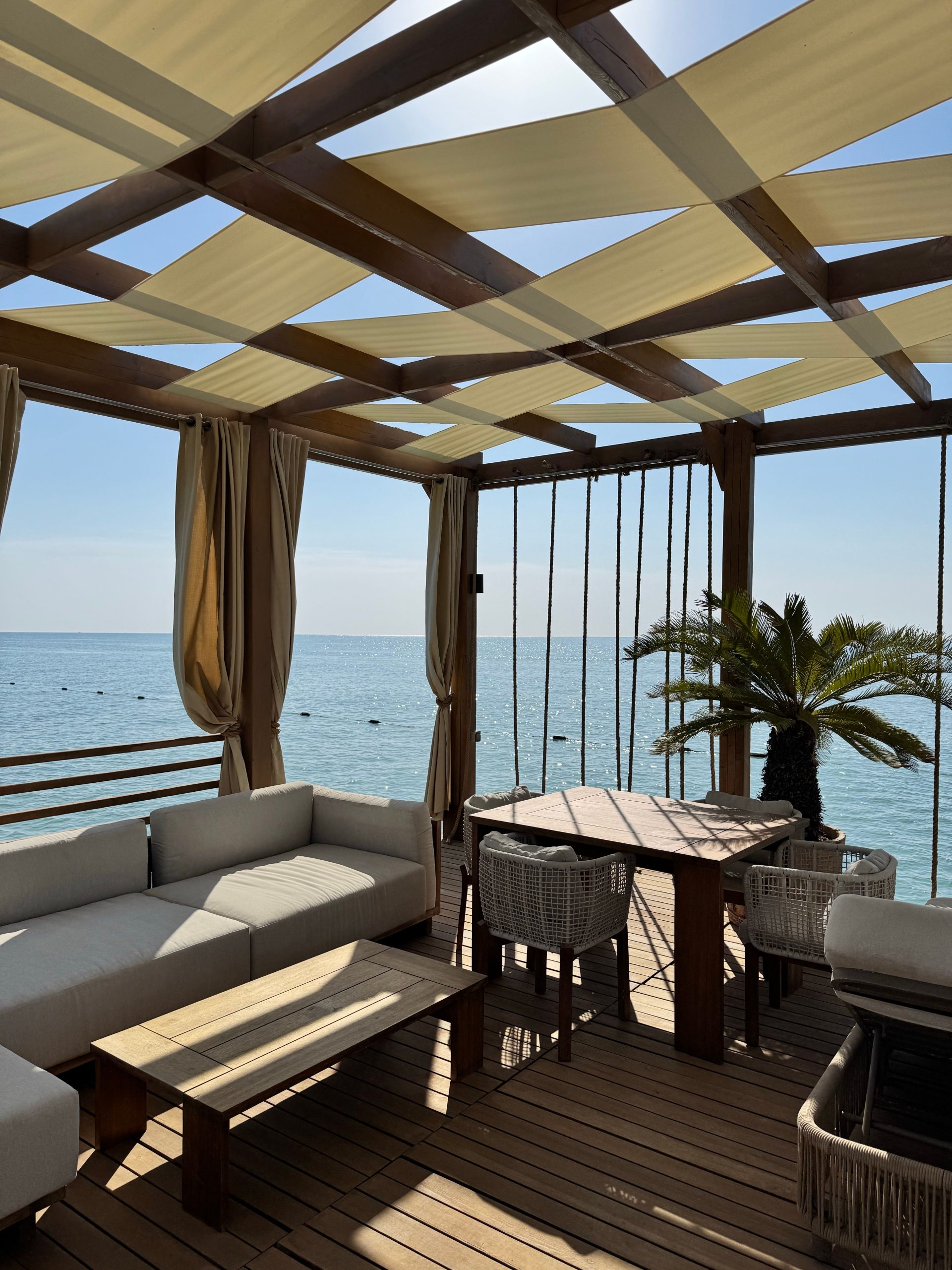 Elegant beachfront outdoor lounge under a pergola with ocean view.