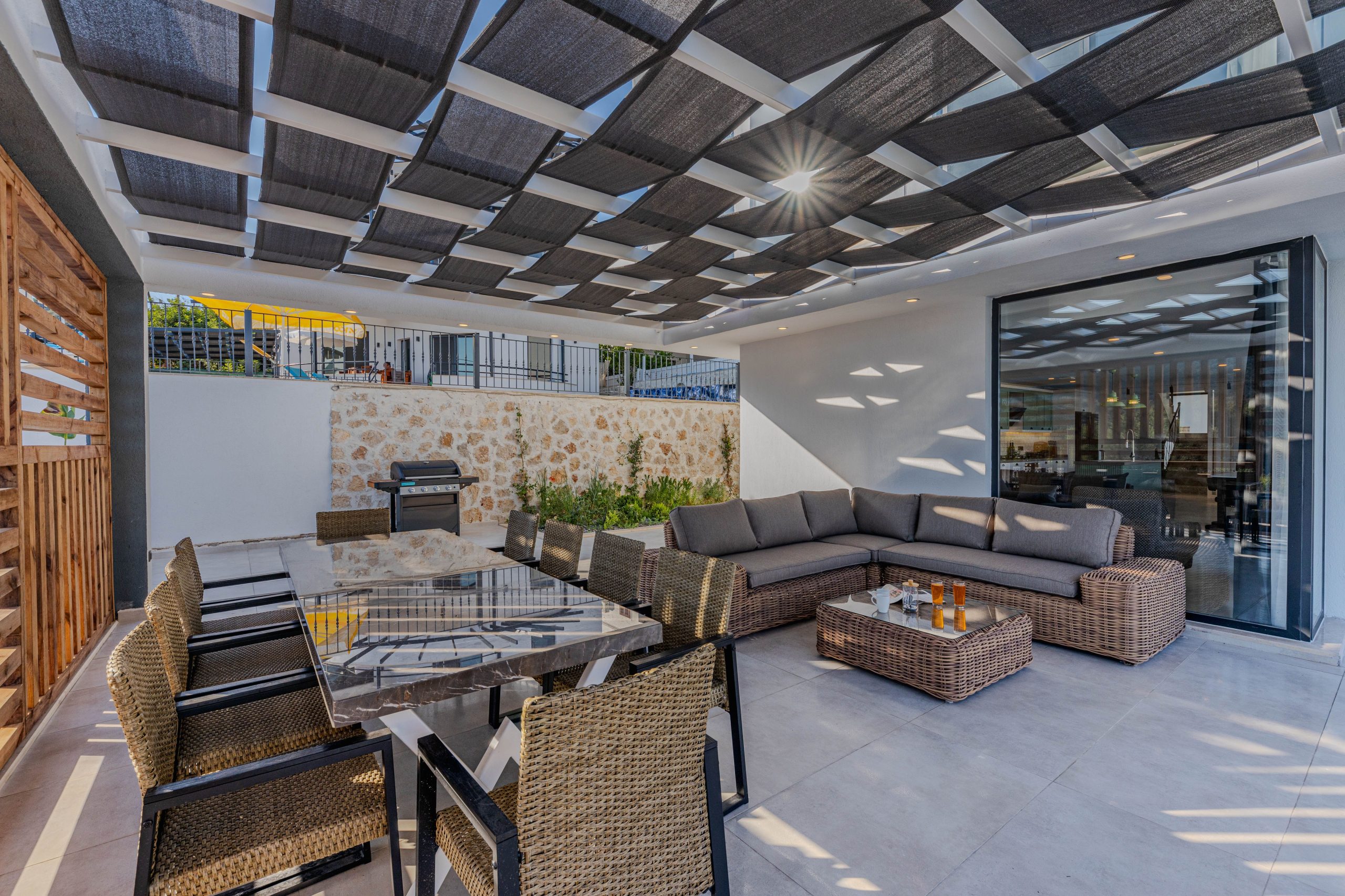 Elegant outdoor patio featuring modern wicker furniture with a sunlit geometric roof.