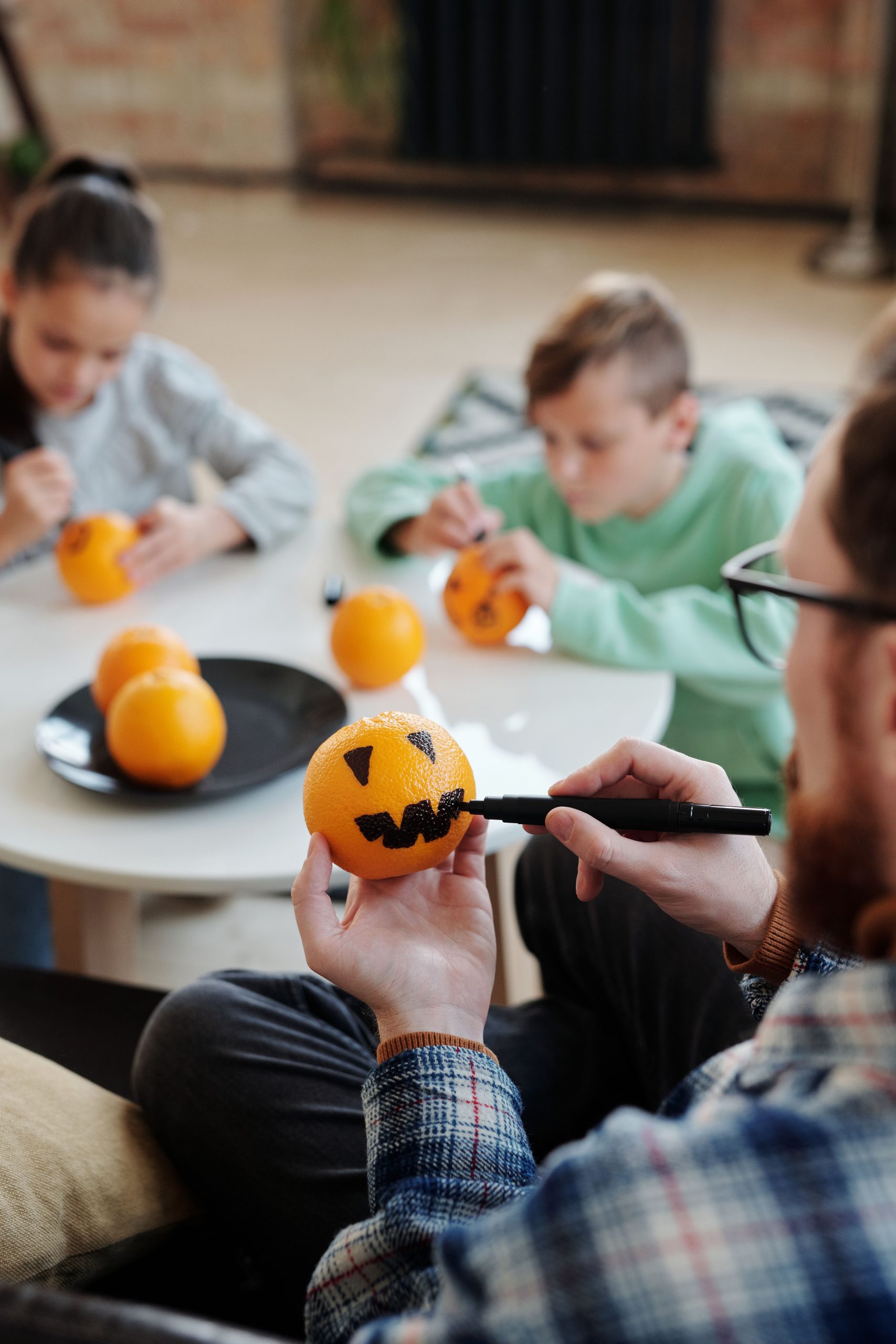 Family decorating oranges as jack-o'-lanterns for a fun Halloween activity at home.