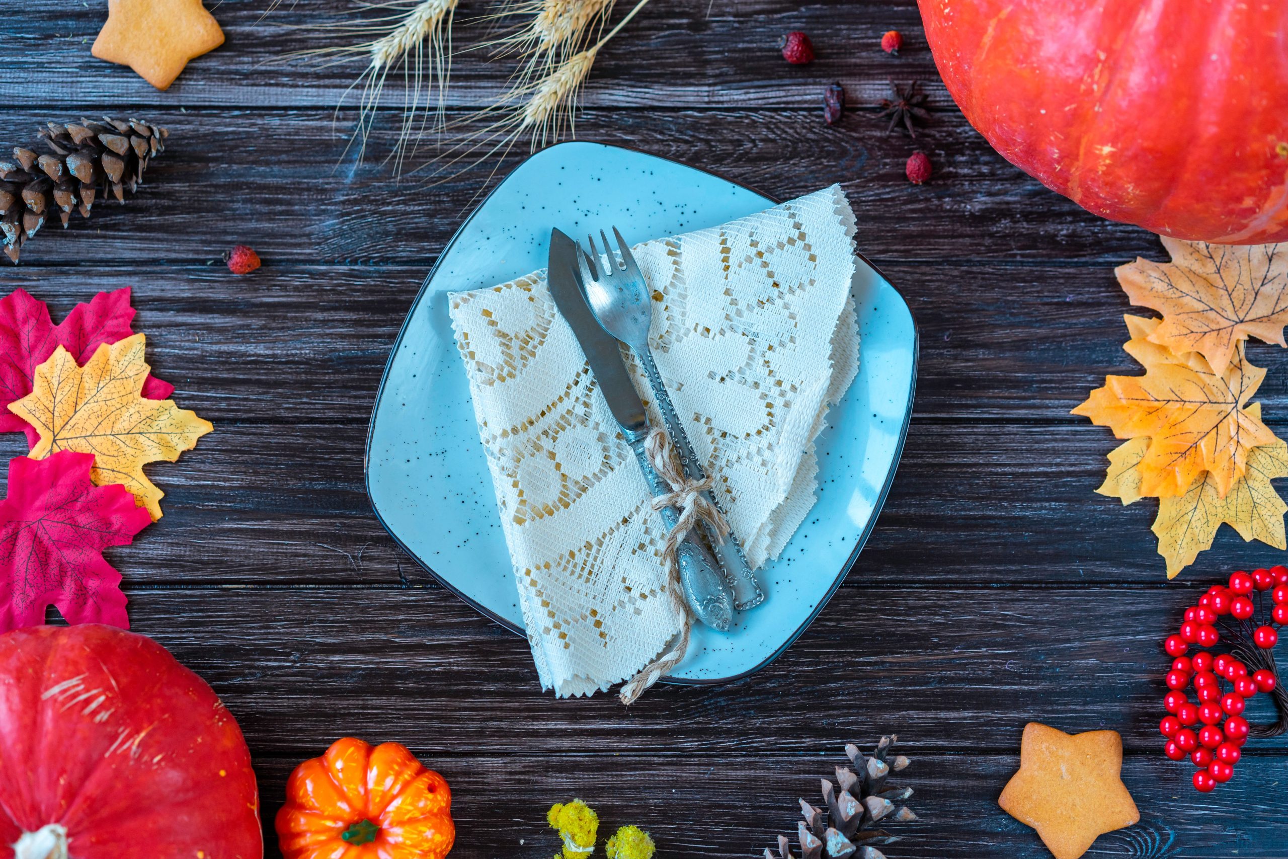 Flat lay of autumn-themed table setting with pumpkins, leaves, and rustic cutlery on wooden background.