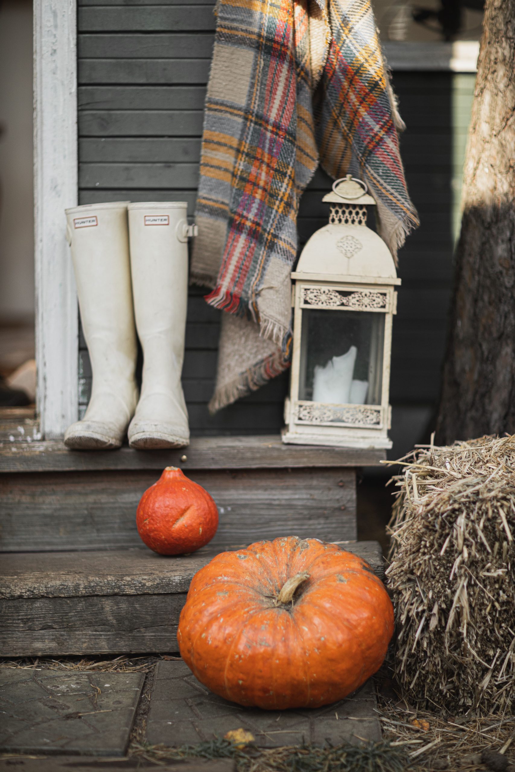Inviting fall scene with pumpkins, boots, lantern, and plaid. Perfect for seasonal decoration ideas.