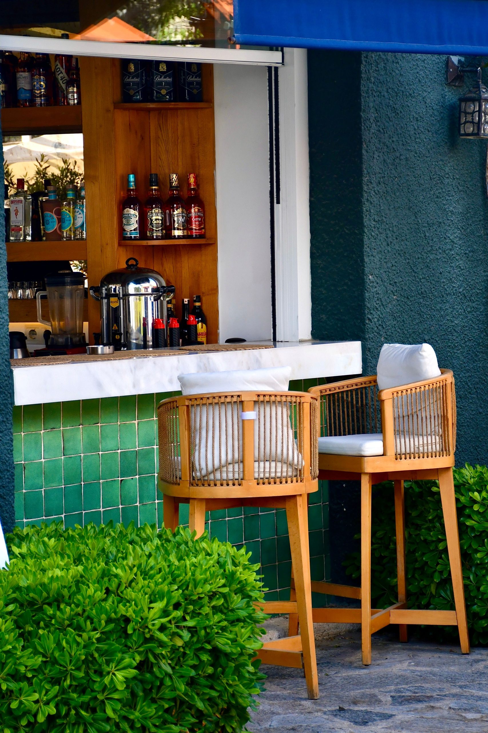 Inviting outdoor bar setup with wicker chairs, green tiles, and lush greenery. Perfect for a relaxed gathering.