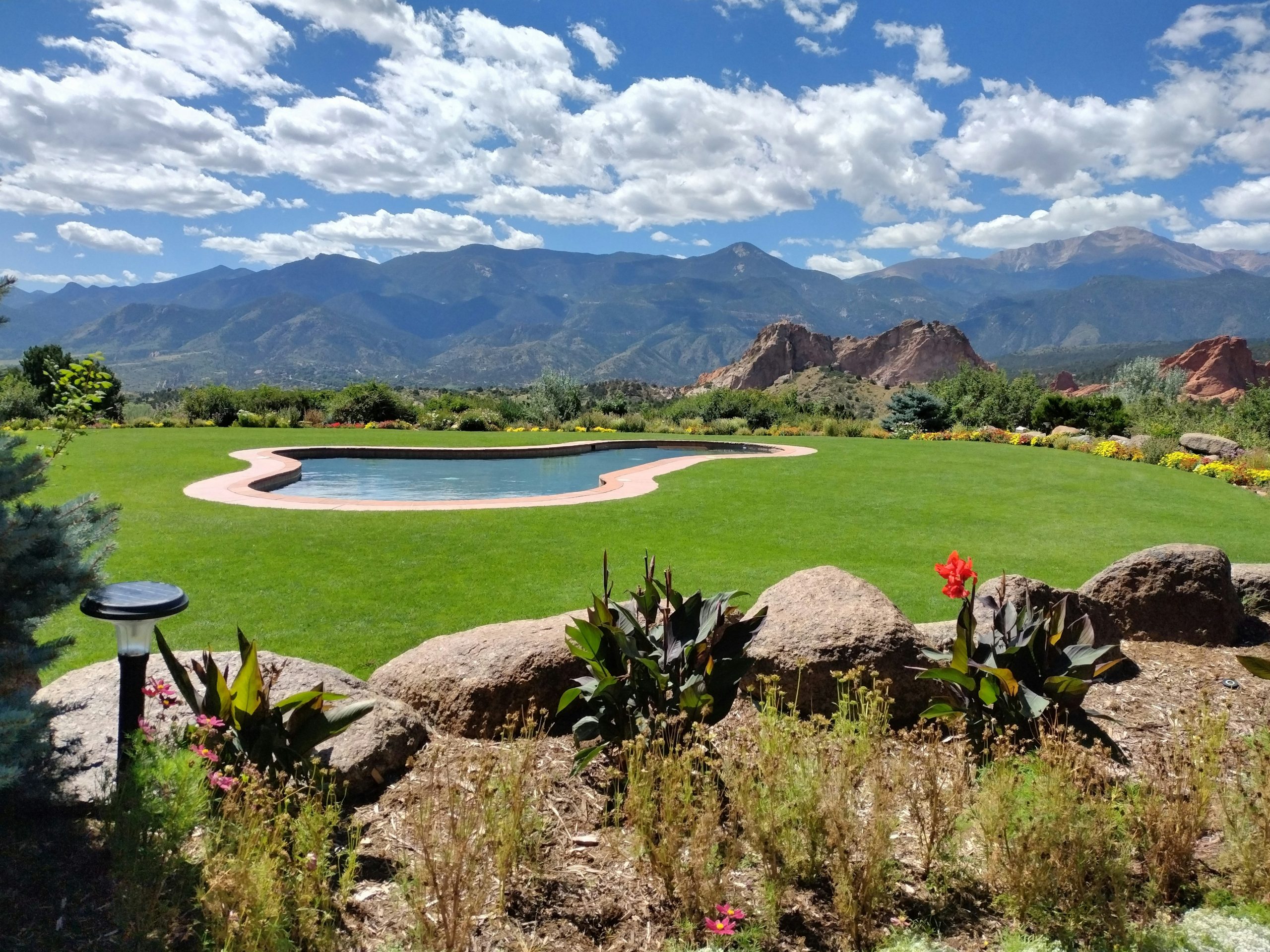 landscape includes beauty and colors of Red Rocks area of Rocky Mountains . pool of water in middle of green grass and cloudy blue sky completes the magnificent summer scene.