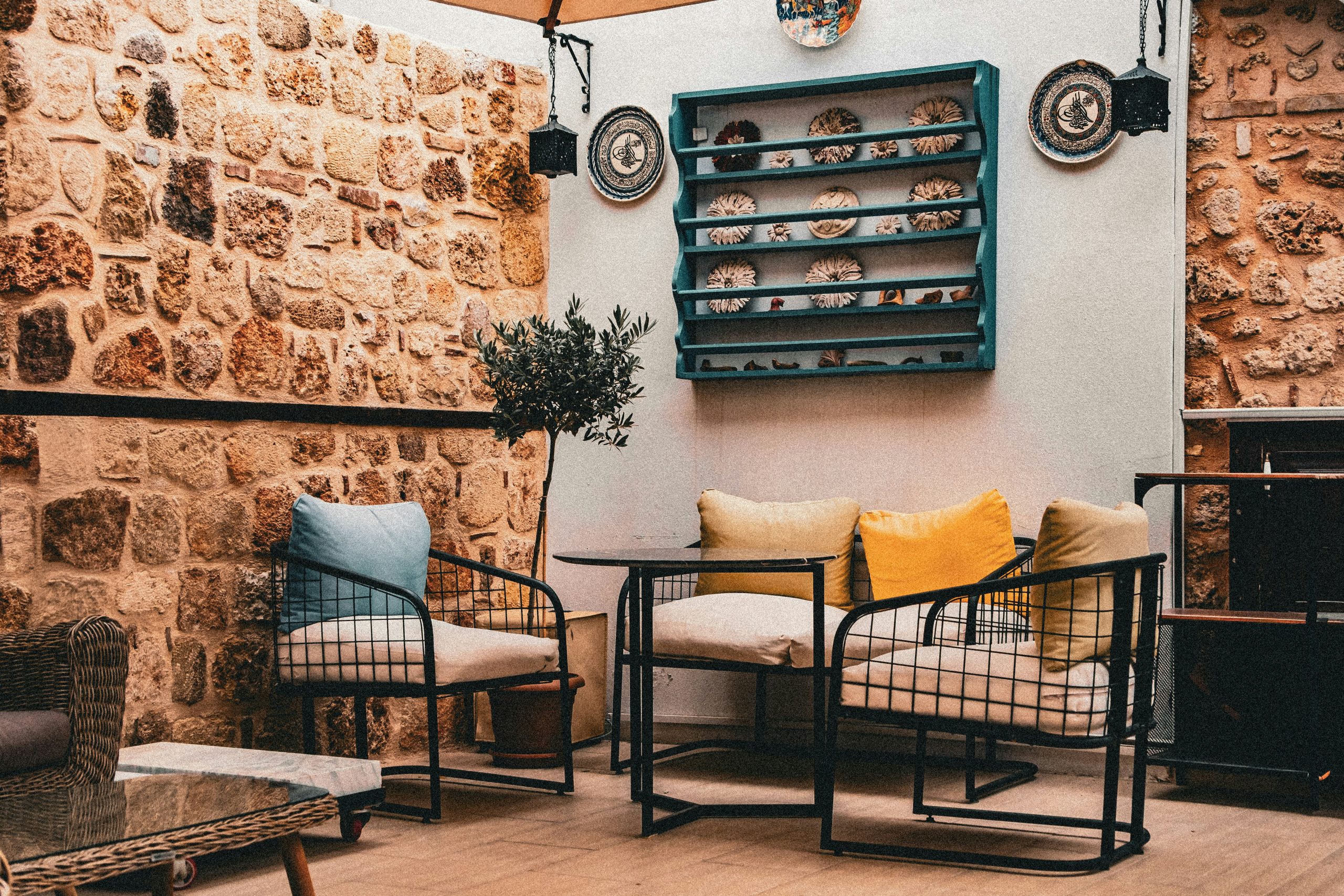 Metal chairs with cushions and a small table against a rustic stone wall