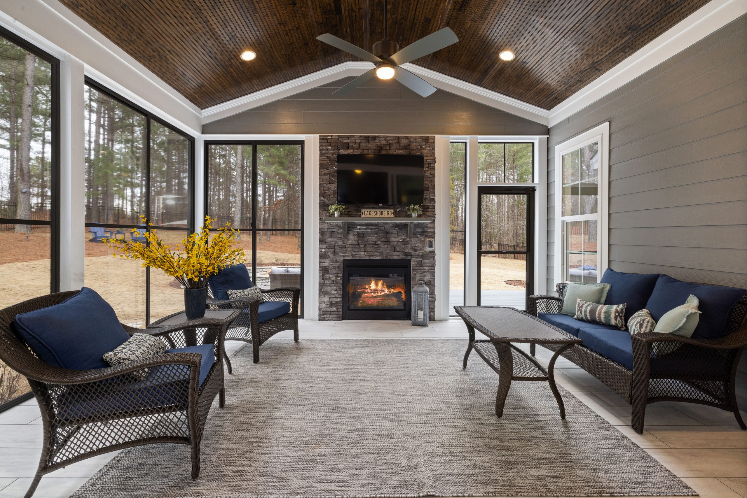 Modern enclosed patio featuring wicker furniture, a fireplace, and large windows with outdoor views.
