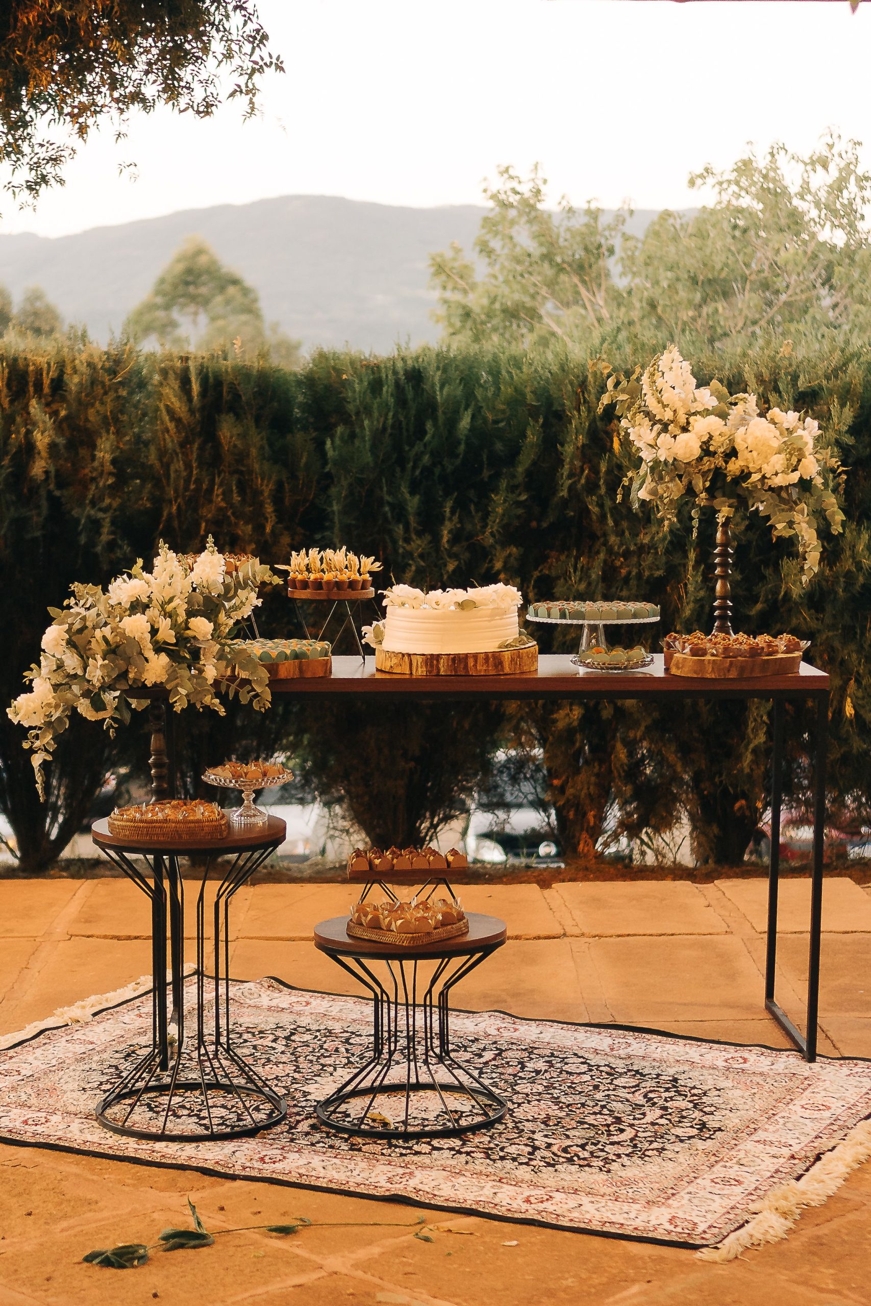 Outdoor wedding dessert table with elegant floral arrangements and diverse pastries.
