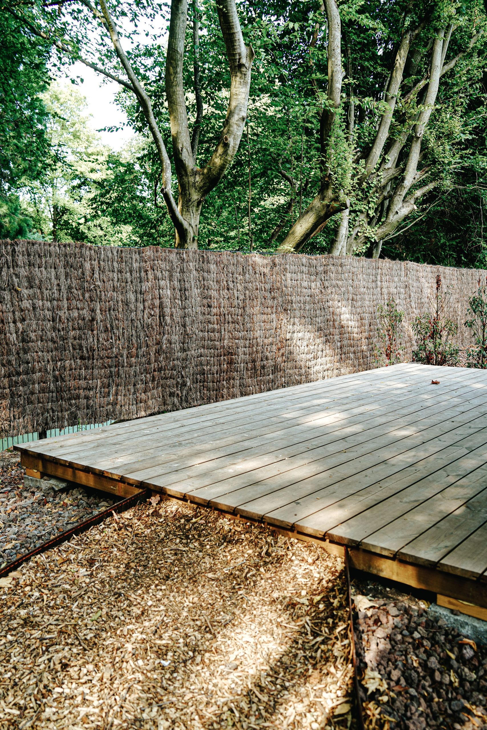 Peaceful wooden deck surrounded by lush green trees and privacy fence.