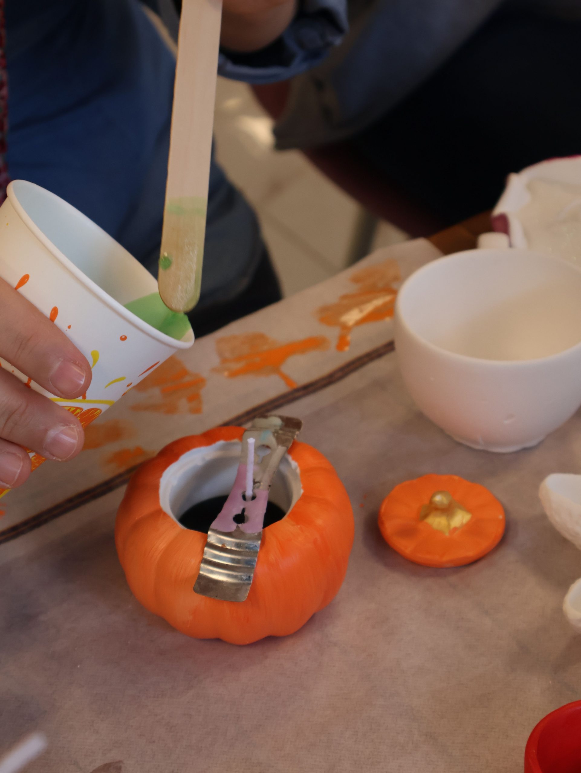 Person decorating mini pumpkin with green paint for Halloween craft.