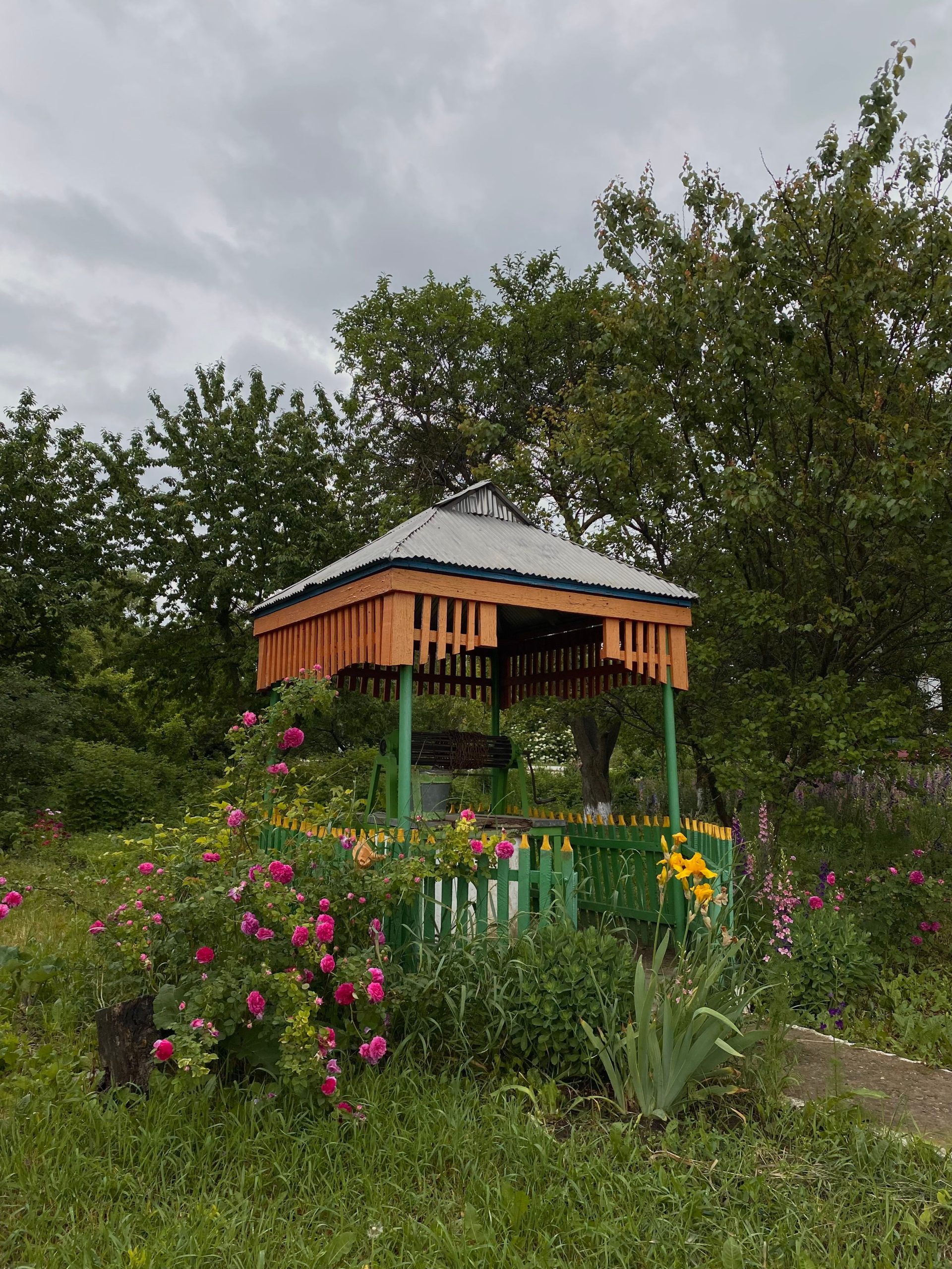 Picturesque gazebo surrounded by vibrant flowers and greenery under a cloudy sky.
