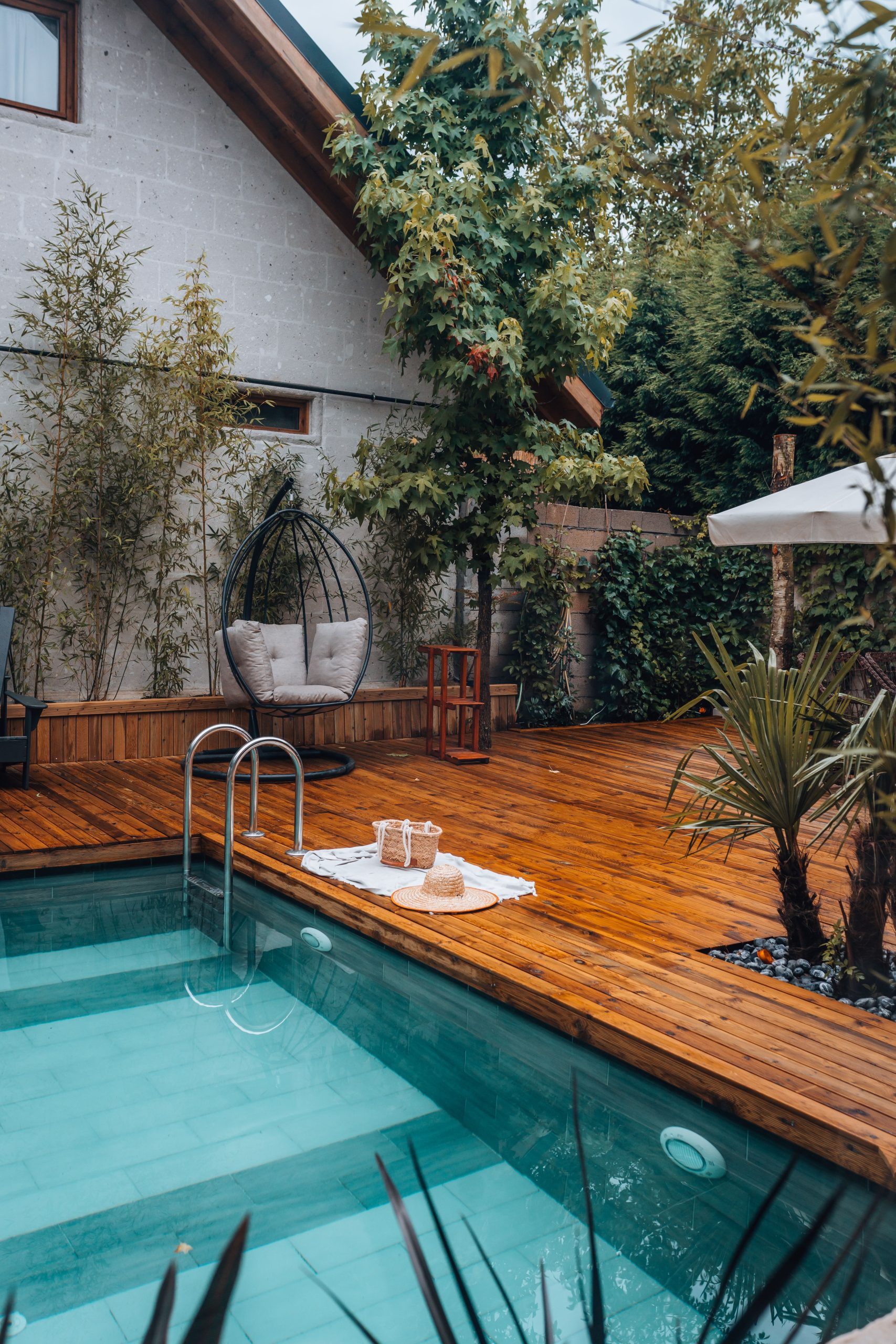 Serene backyard retreat with pool, wooden deck, and lush greenery.