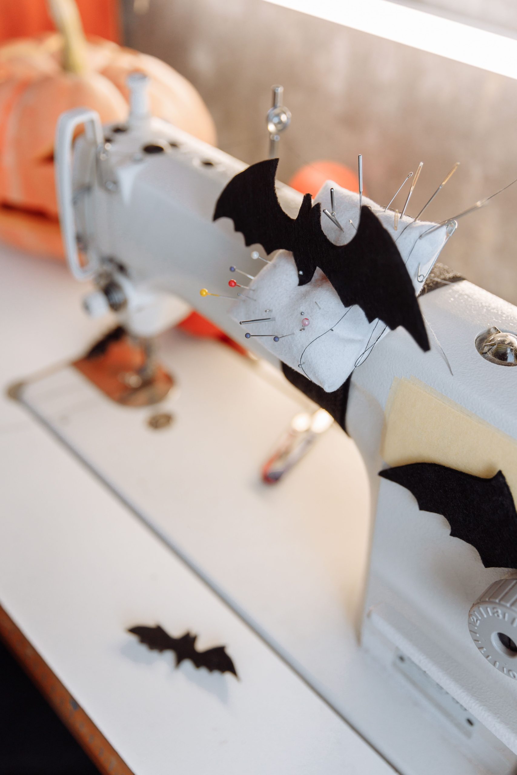 Sewing machine adorned with bat decorations, pumpkins in the background, perfect for Halloween crafts.