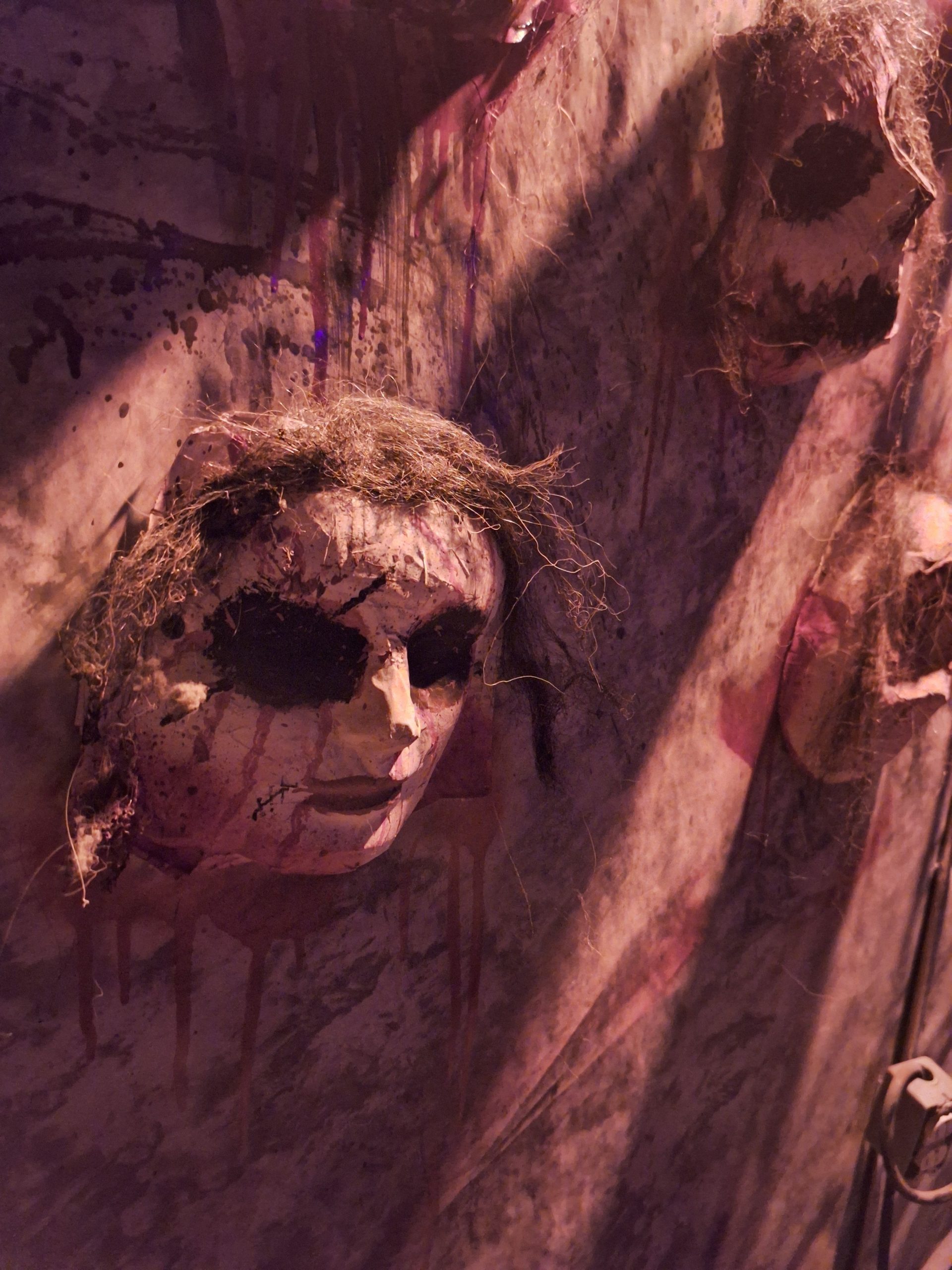 Spooky display of eerie masks on a wall casting haunting shadows in dim light.