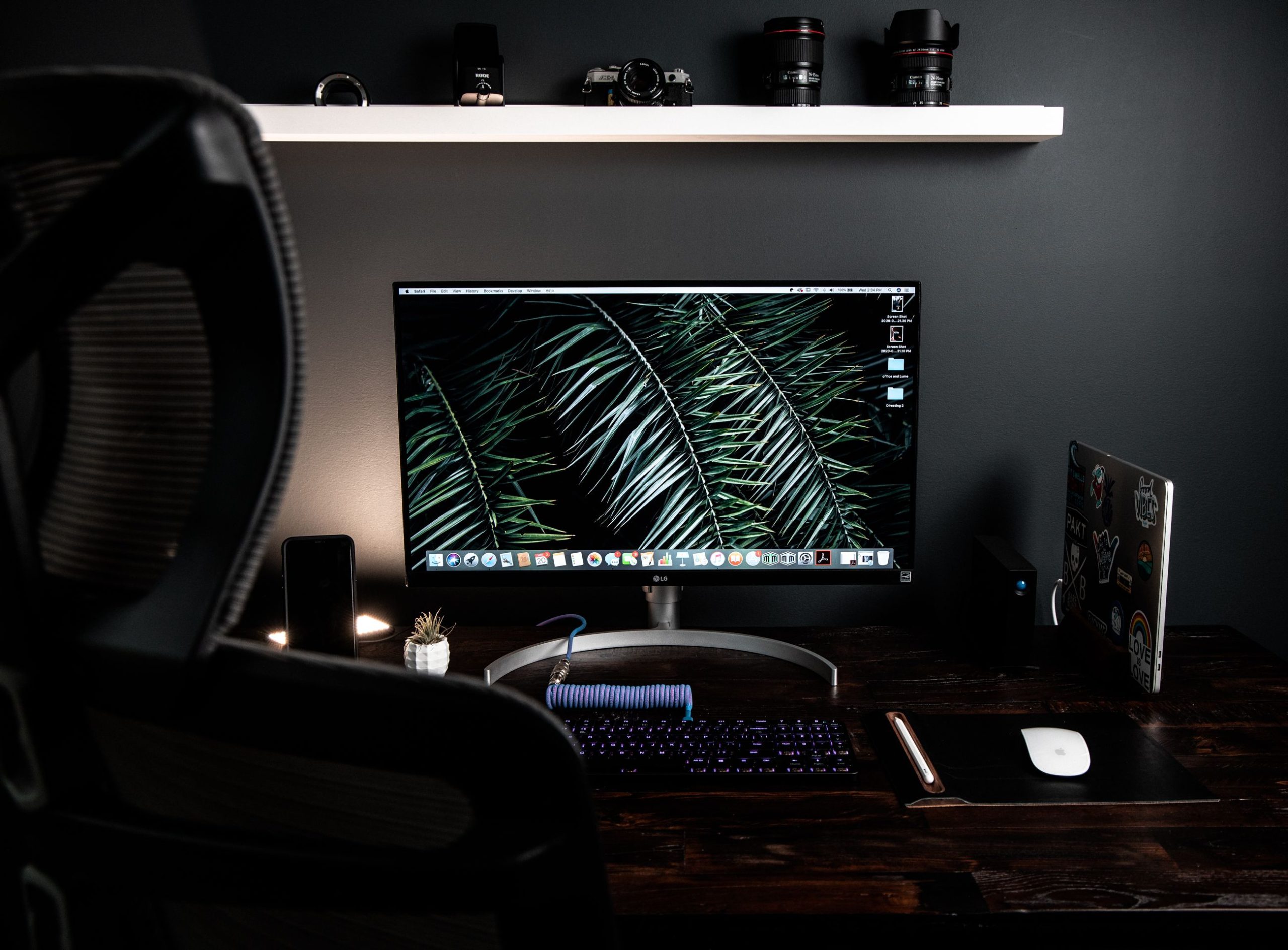 Stationery computer with keyboard and mouse on desk placed under white shelf in dark workspace with armchair near table in modern room