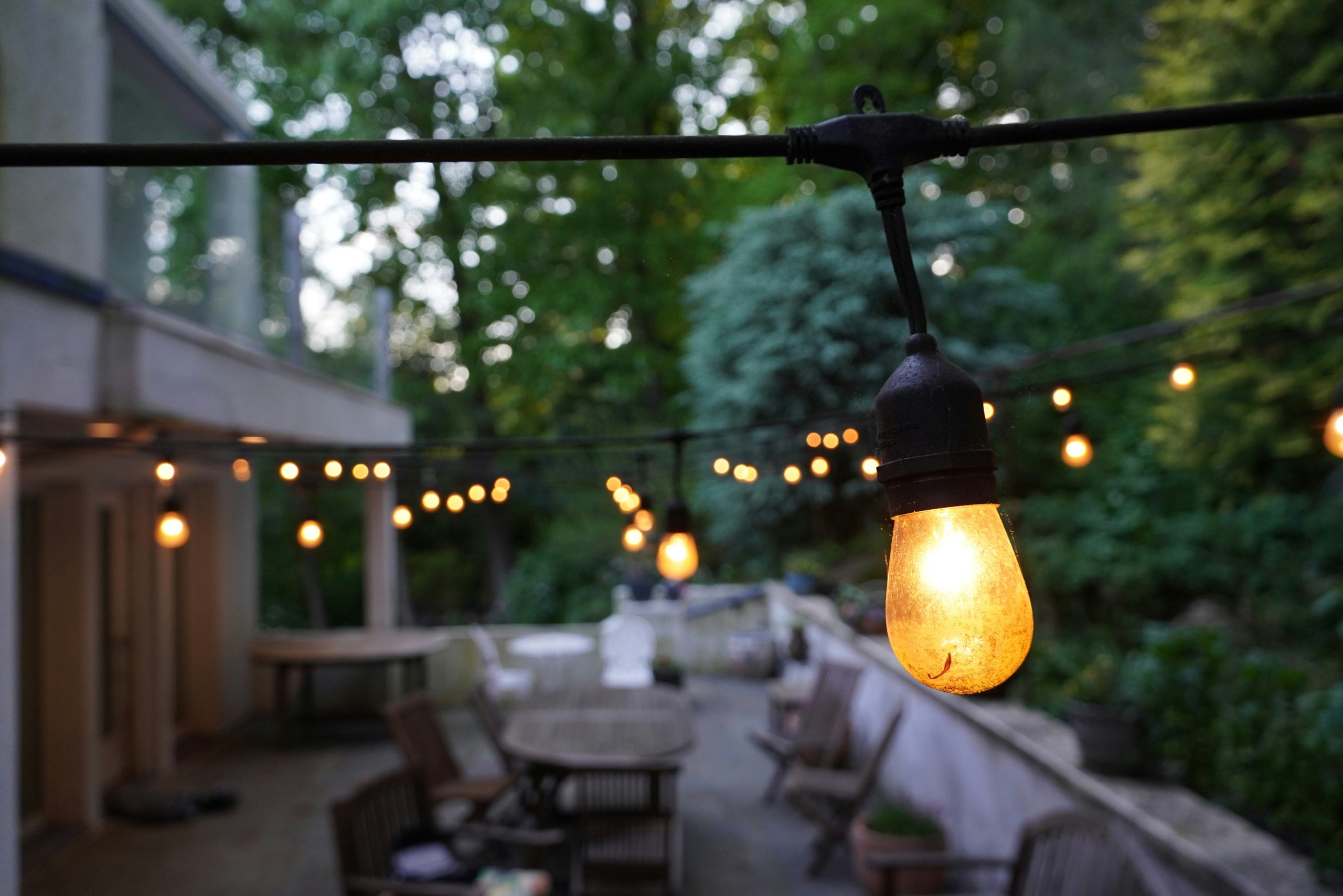 String lights illuminate an outdoor patio with tables and chairs