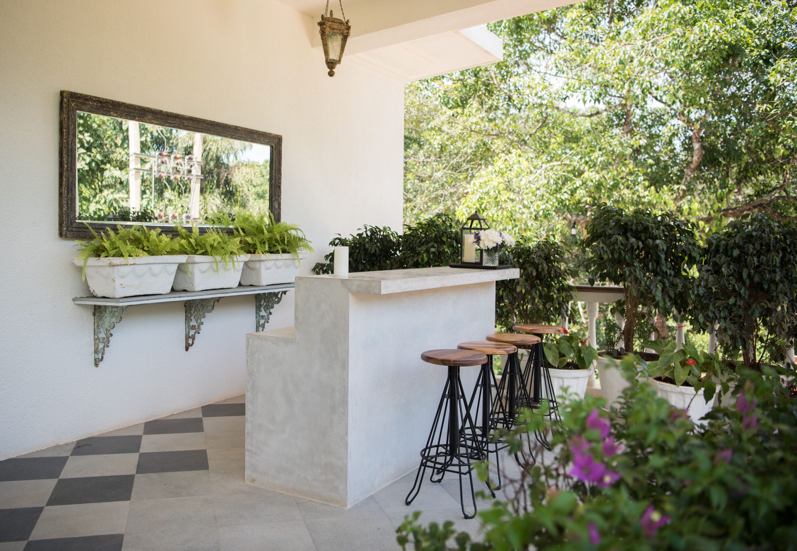 Stylish outdoor bar with stools and lush greenery, perfect for relaxation in a garden setting.