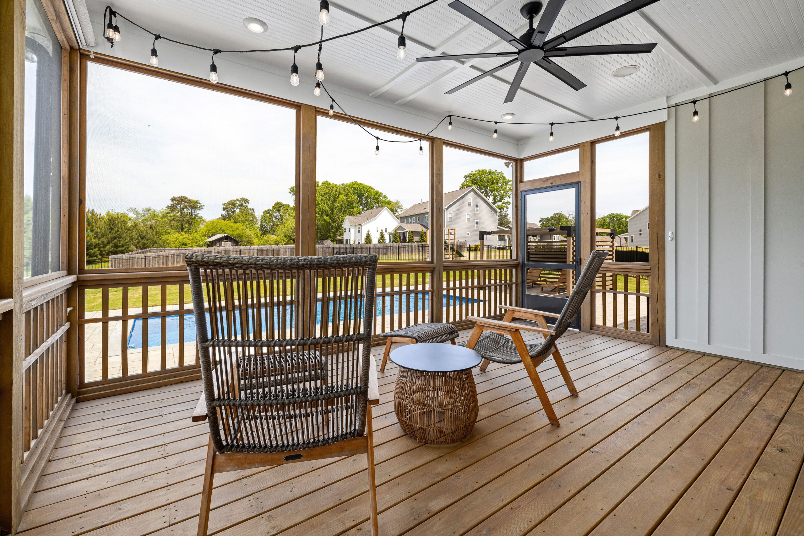 Stylish screened terrace with wooden furniture and ceiling fan, overlooking a serene backyard pool.