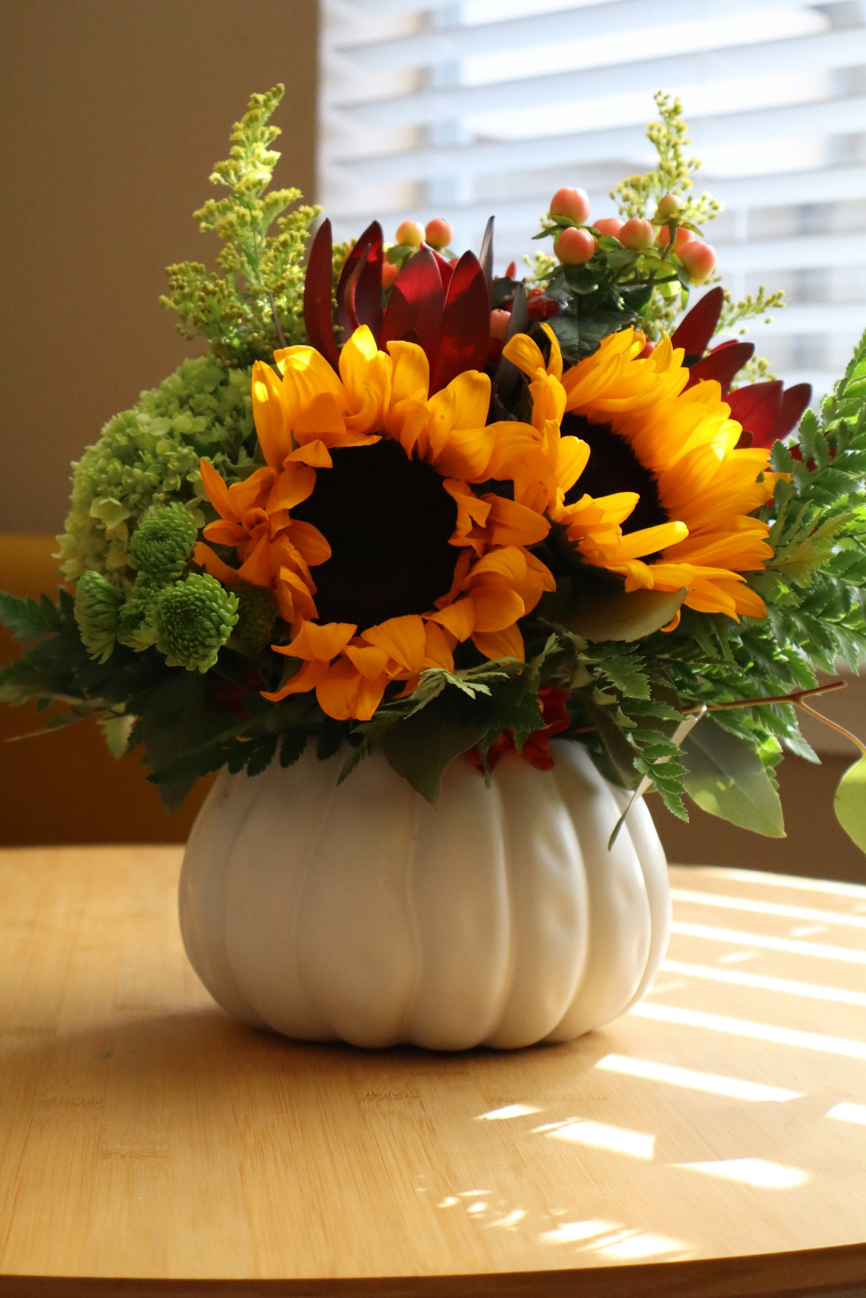 Sunflowers and green hydrangeas in a white pumpkin vase on a wooden table