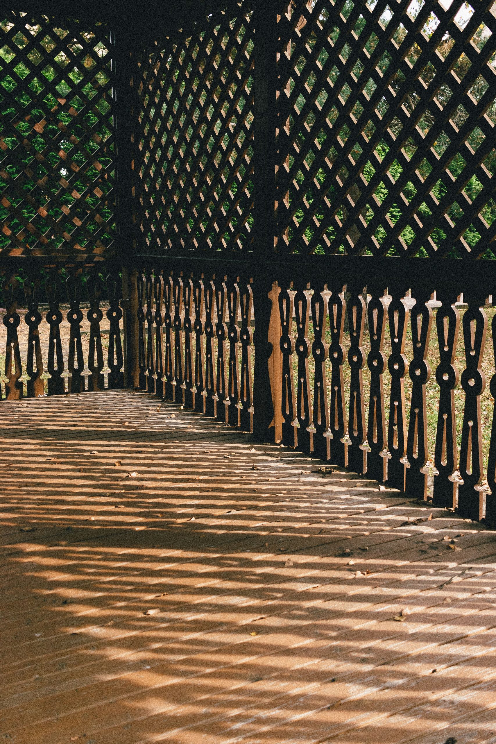 Sunlight creates intricate geometric patterns on a wooden patio, casting shadows through lattice fencing.