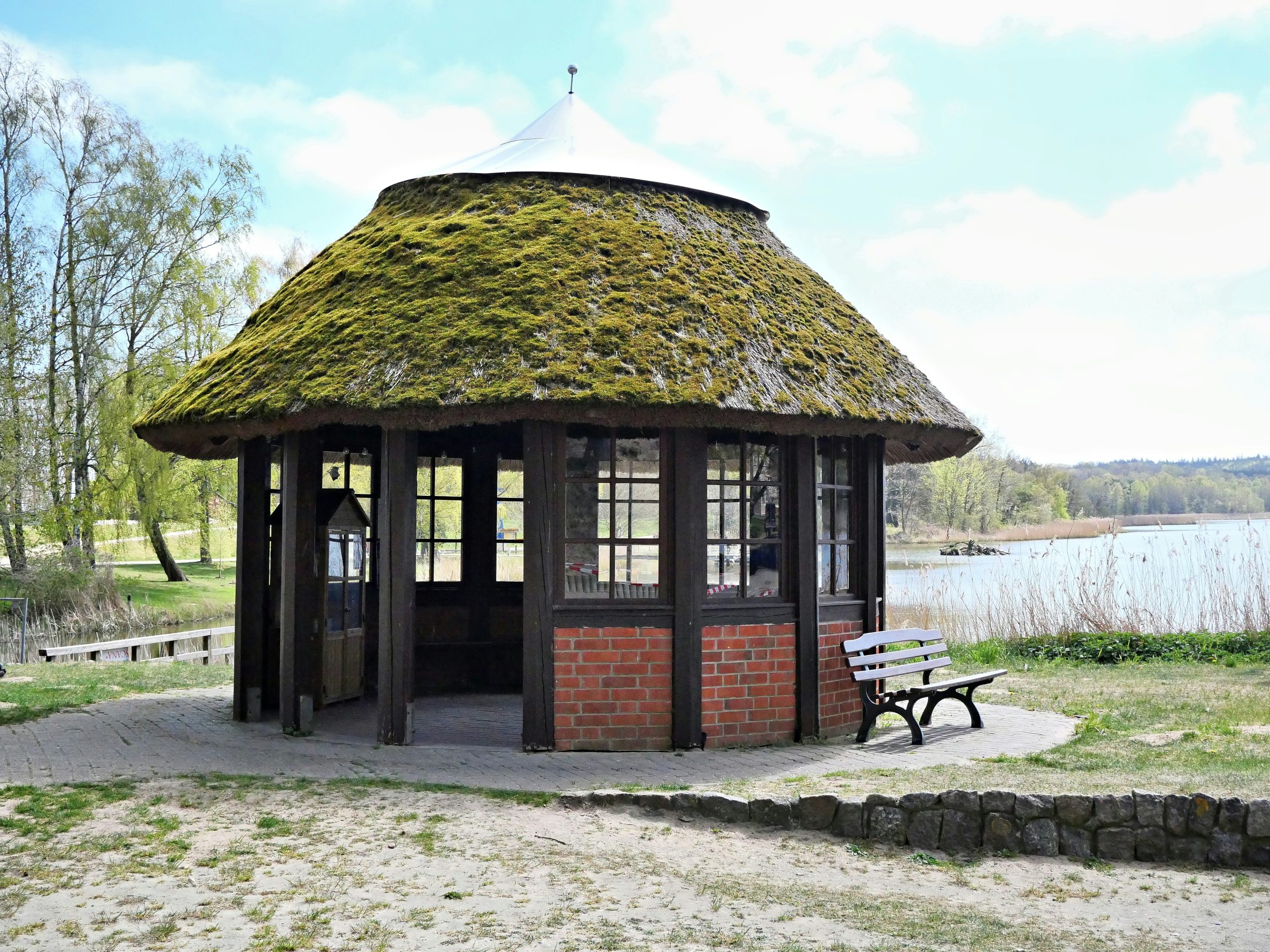 Thatched roof gazebo by a calm lake with a bench