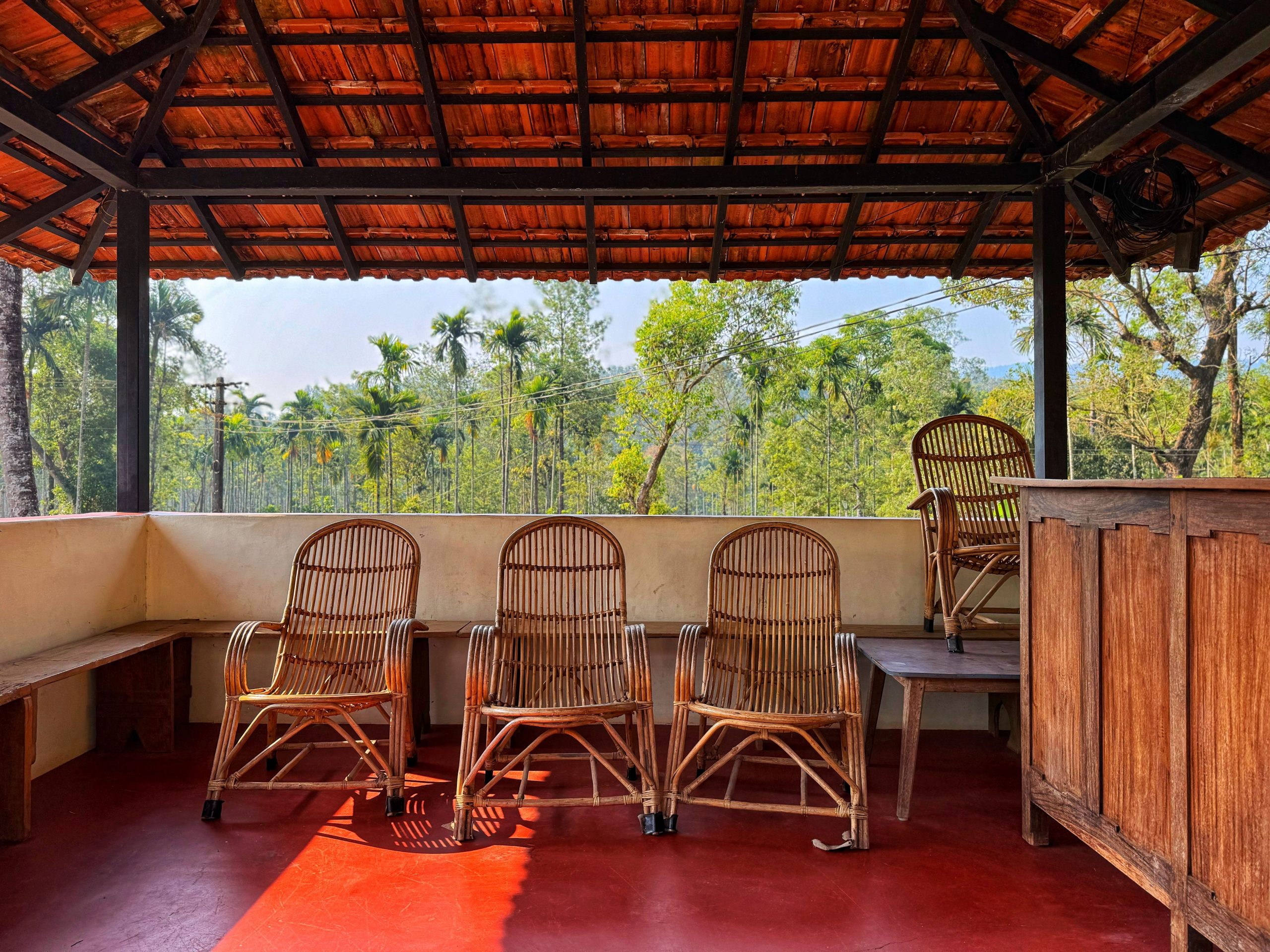 Three rattan chairs in a tropical gazebo with lush greenery view.