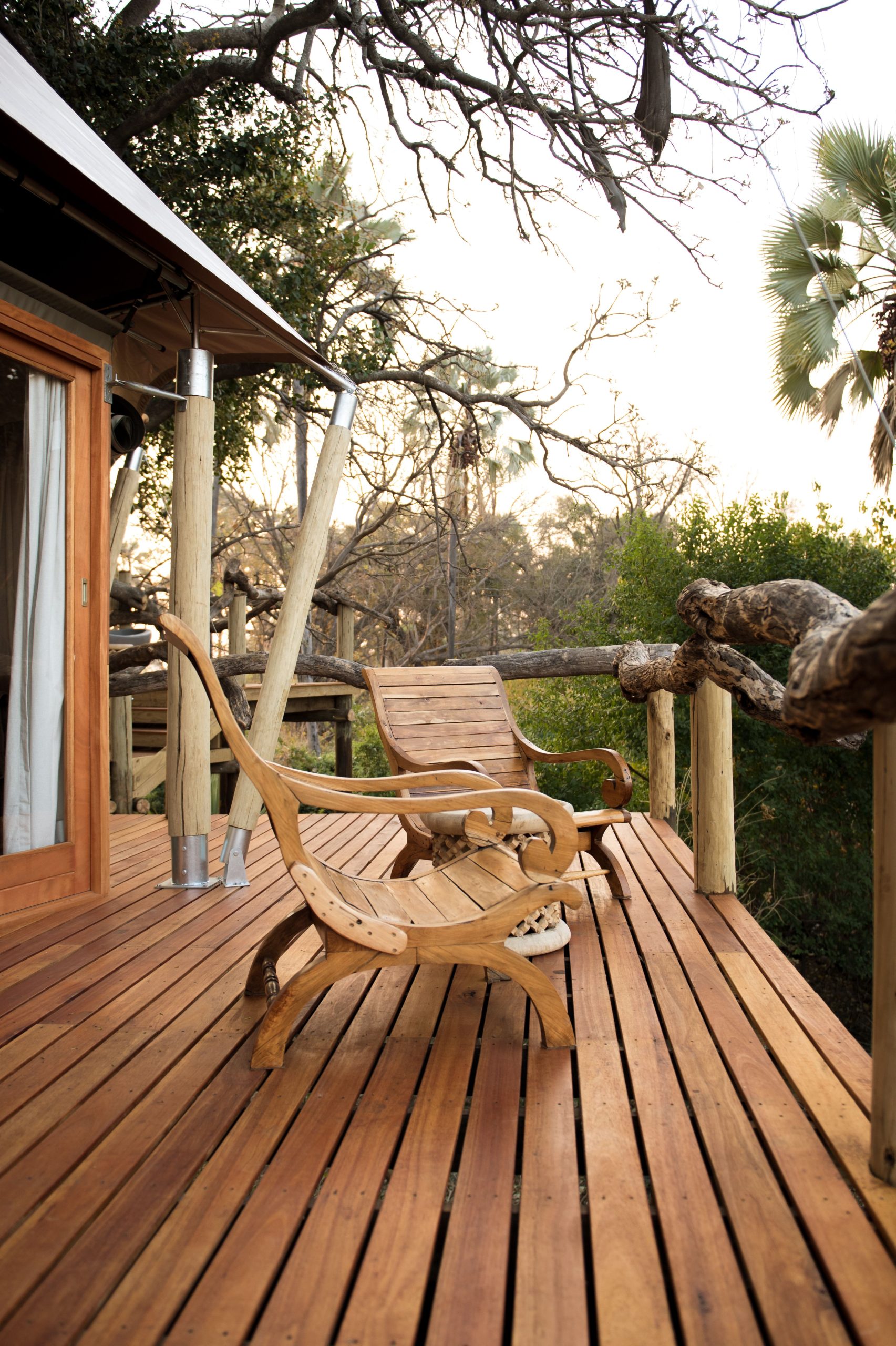 Two wooden chairs on a rustic deck surrounded by lush nature.