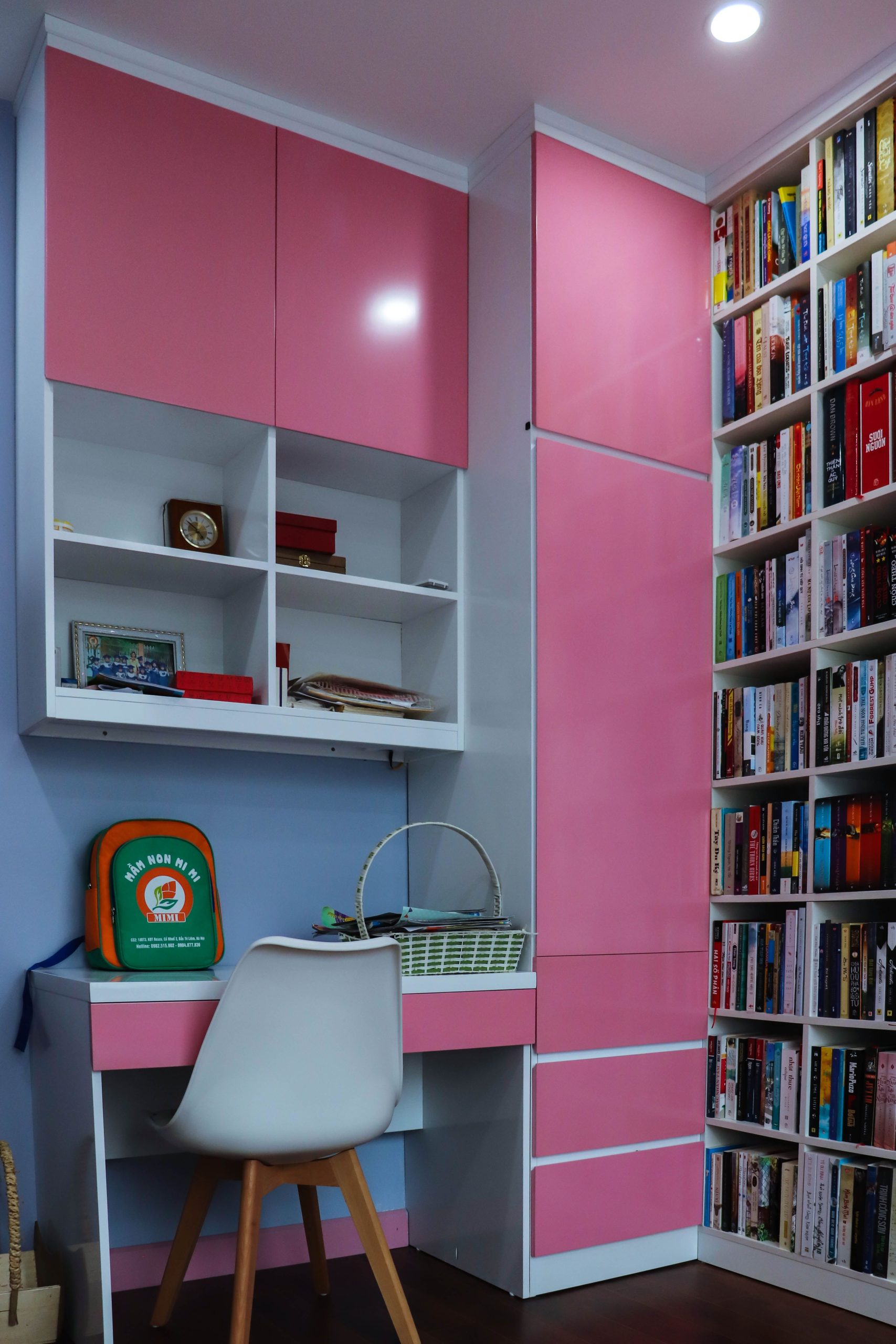 Vibrant home office setup with pink cabinets, a desk, and a filled bookshelf.