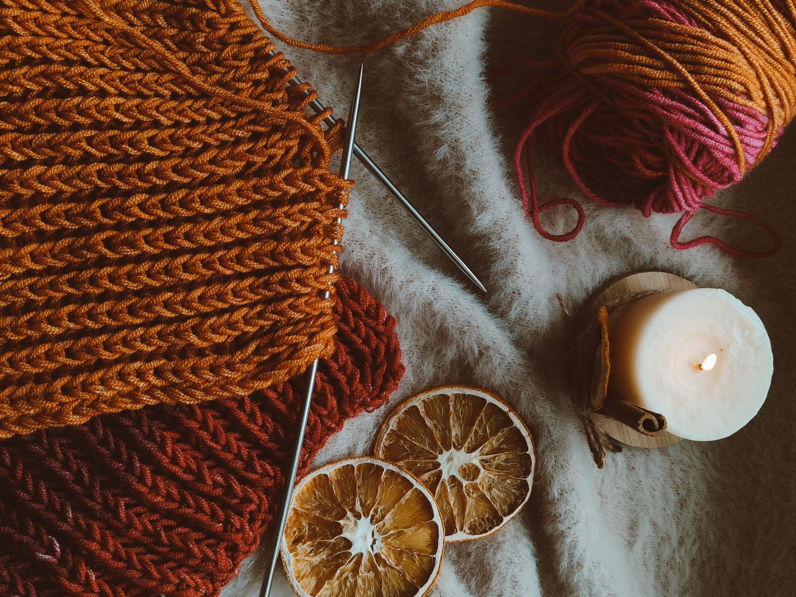 Warm knitted fabric with yarn, knitting needles, candle, and dried oranges on soft fur.