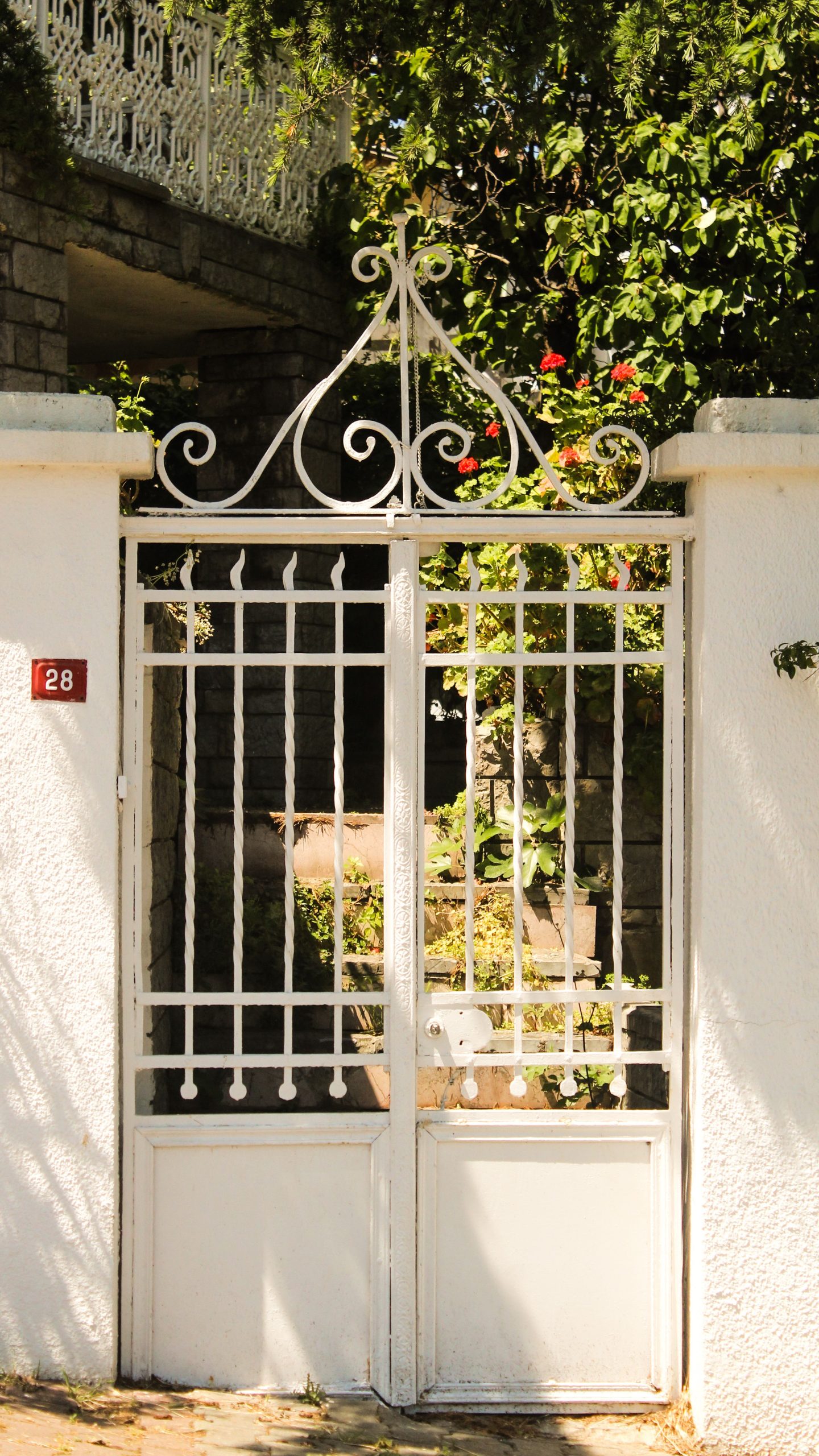 White wrought iron gate adorned with plants under sunlight, giving an inviting atmosphere.