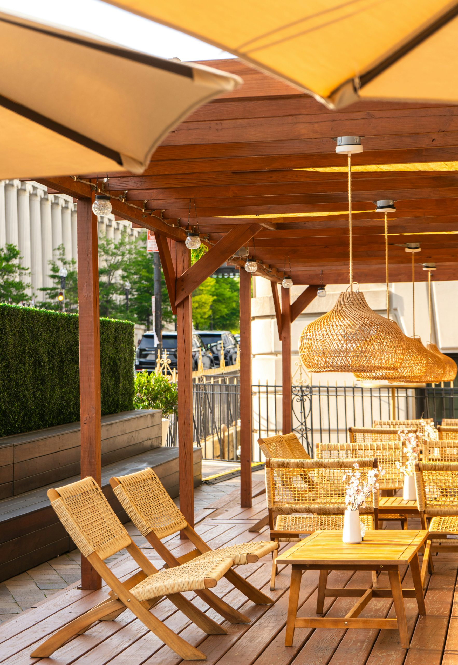Wicker chairs and wooden tables on an outdoor patio with hanging woven lamps