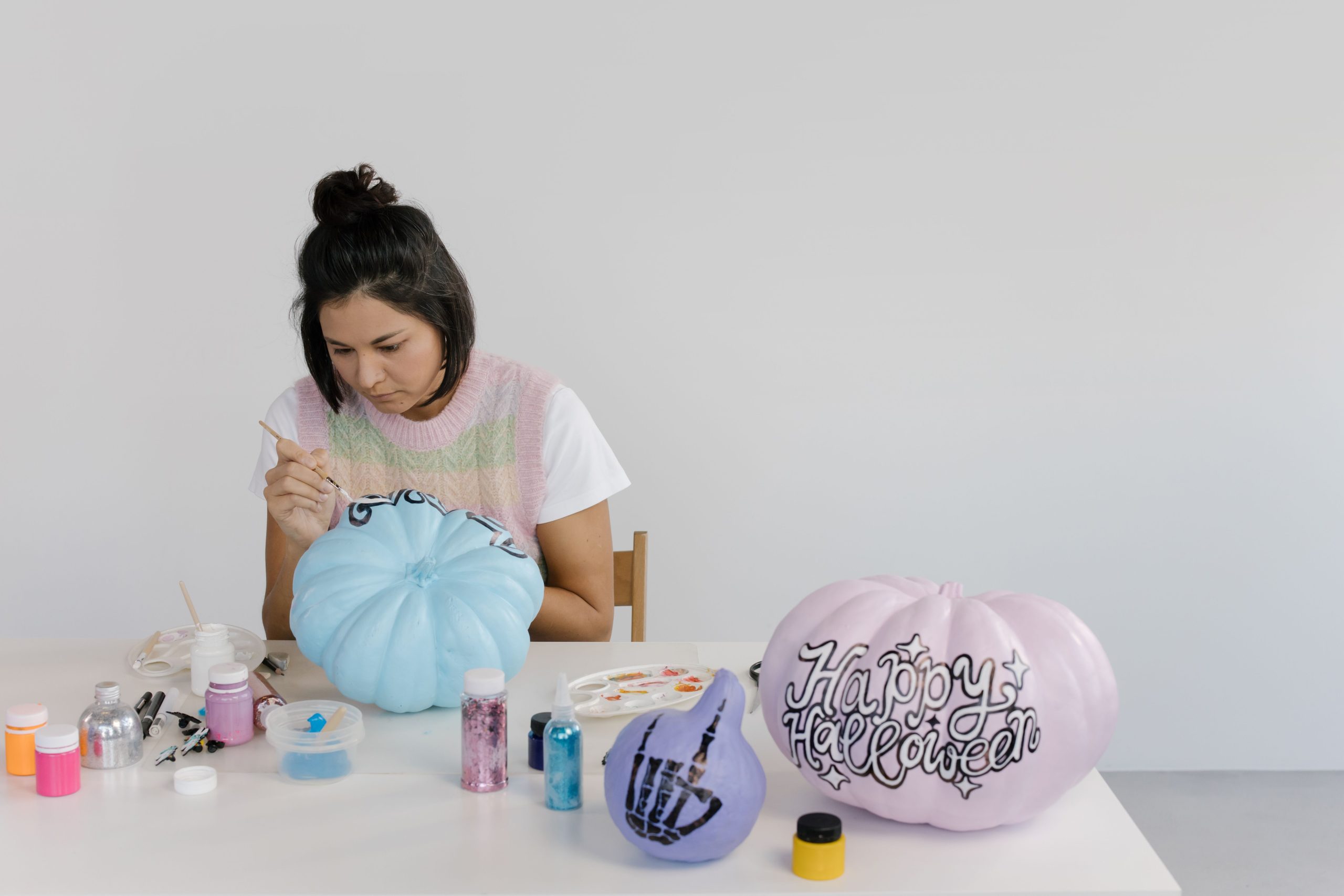 Woman painting pumpkins for Halloween with art supplies on a table.