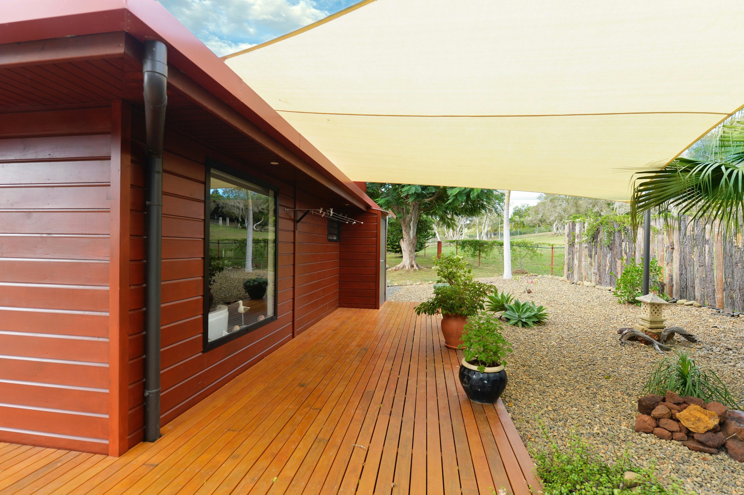 Wooden house with deck, shade sail, and gravel garden