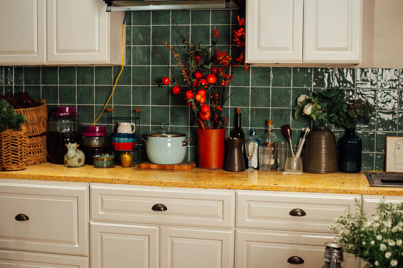 A charming kitchen counter featuring decorative items and utensils against a green tile backsplash.