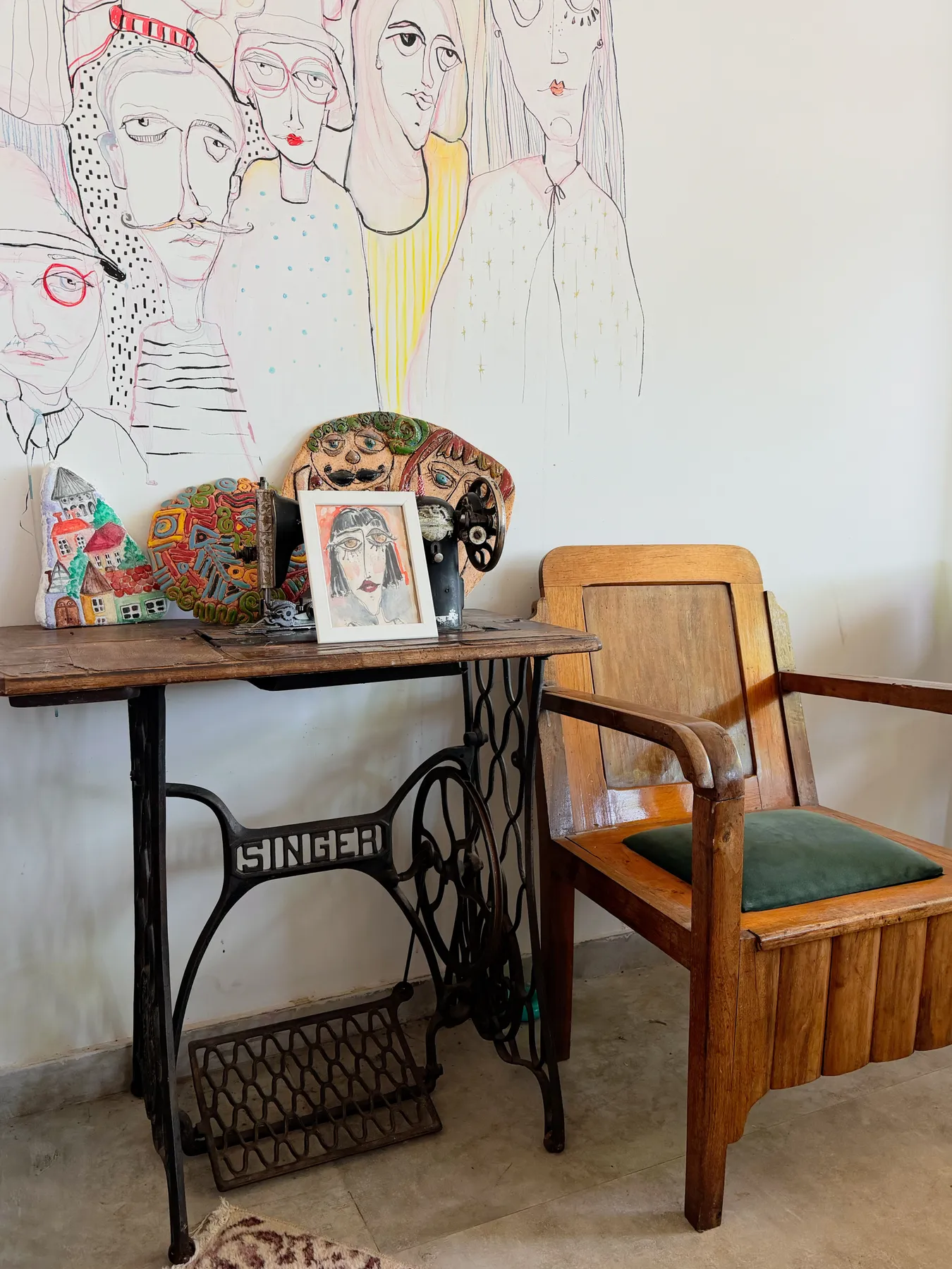 A cozy vintage sewing corner featuring a Singer table and artistic wall mural, perfect for eclectic interiors.
