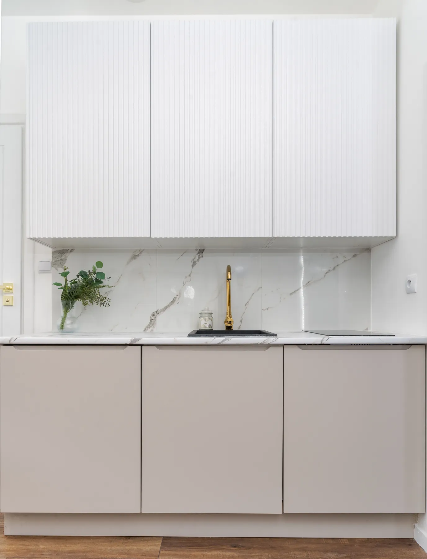 A luxurious minimalist kitchen features marble backsplash and golden faucet.