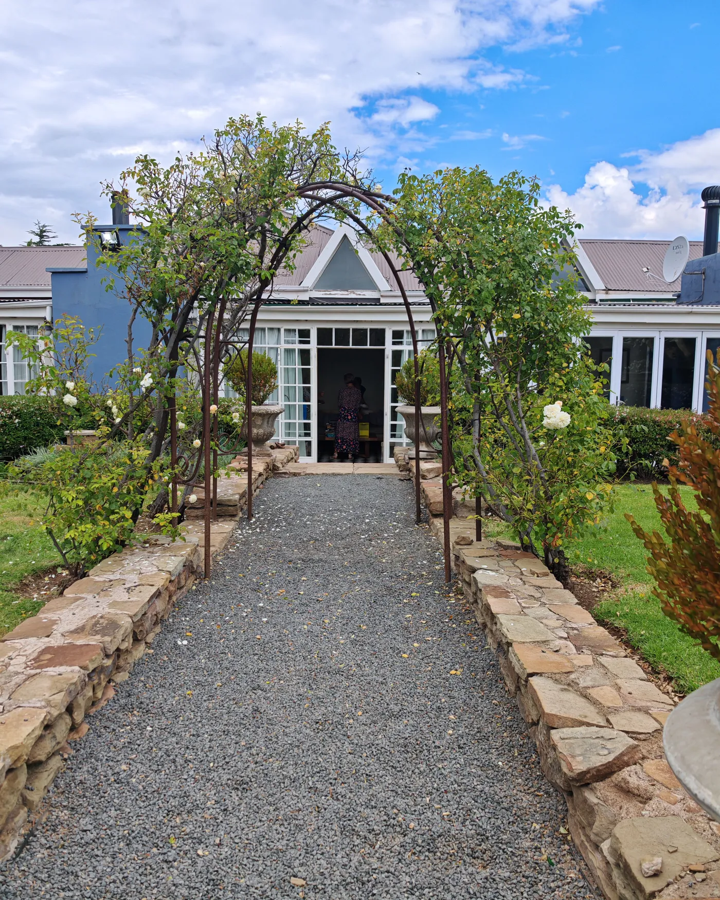 Beautiful garden archway leading to a quaint house entrance under a partly cloudy sky.