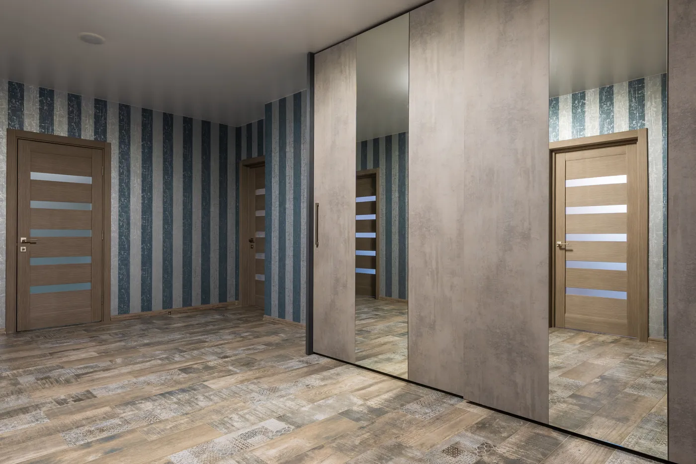 Big wardrobe with reflection in mirrors placed on laminate in spacious hallway of modern apartment with striped wallpaper and doors