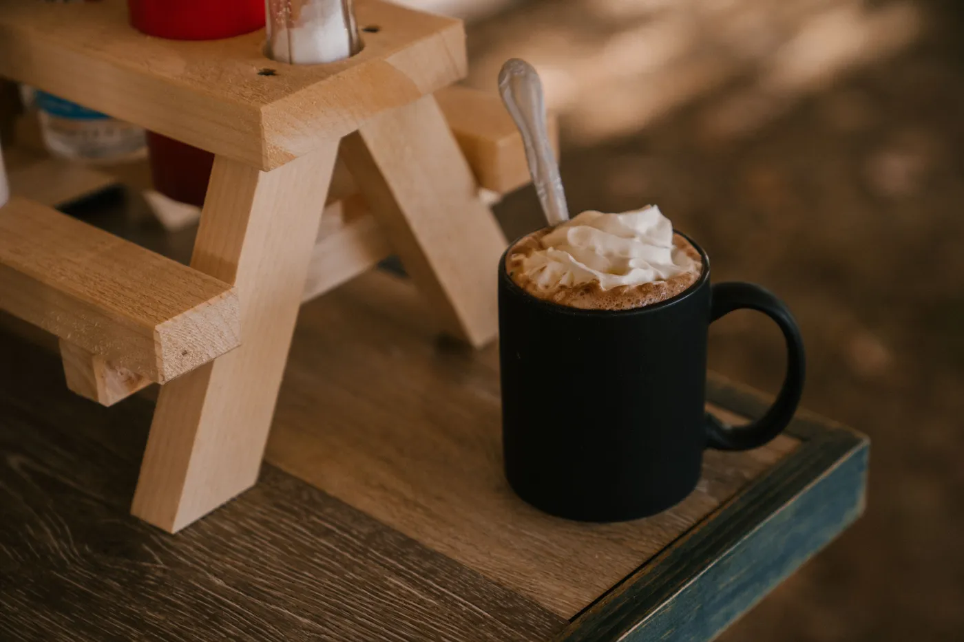 Black cup of aromatic cocoa with whipped cream standing on edge of wooden table