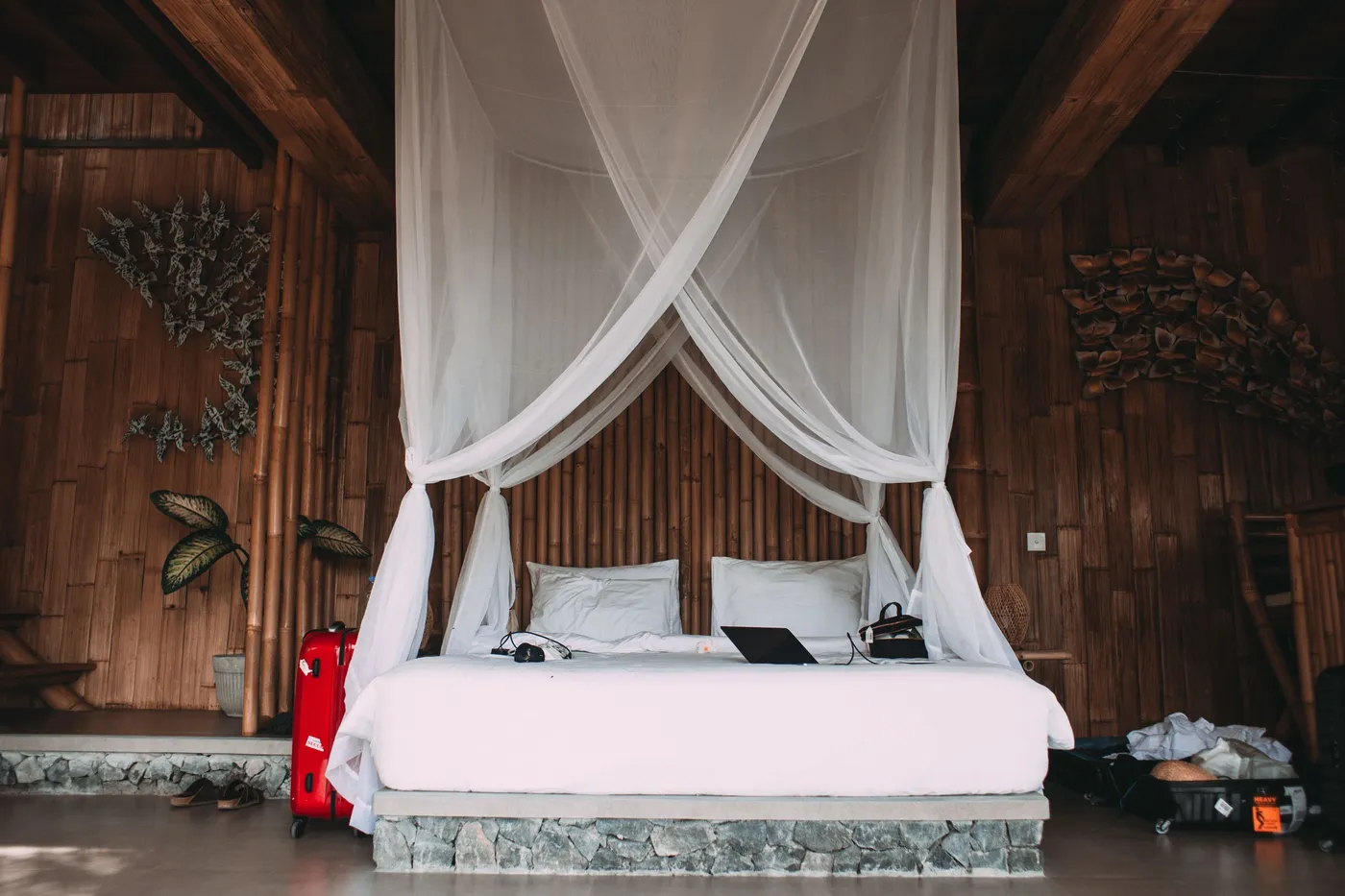 Comfortable bed with netbook and headphones near suitcases and bamboo walls in hotel room
