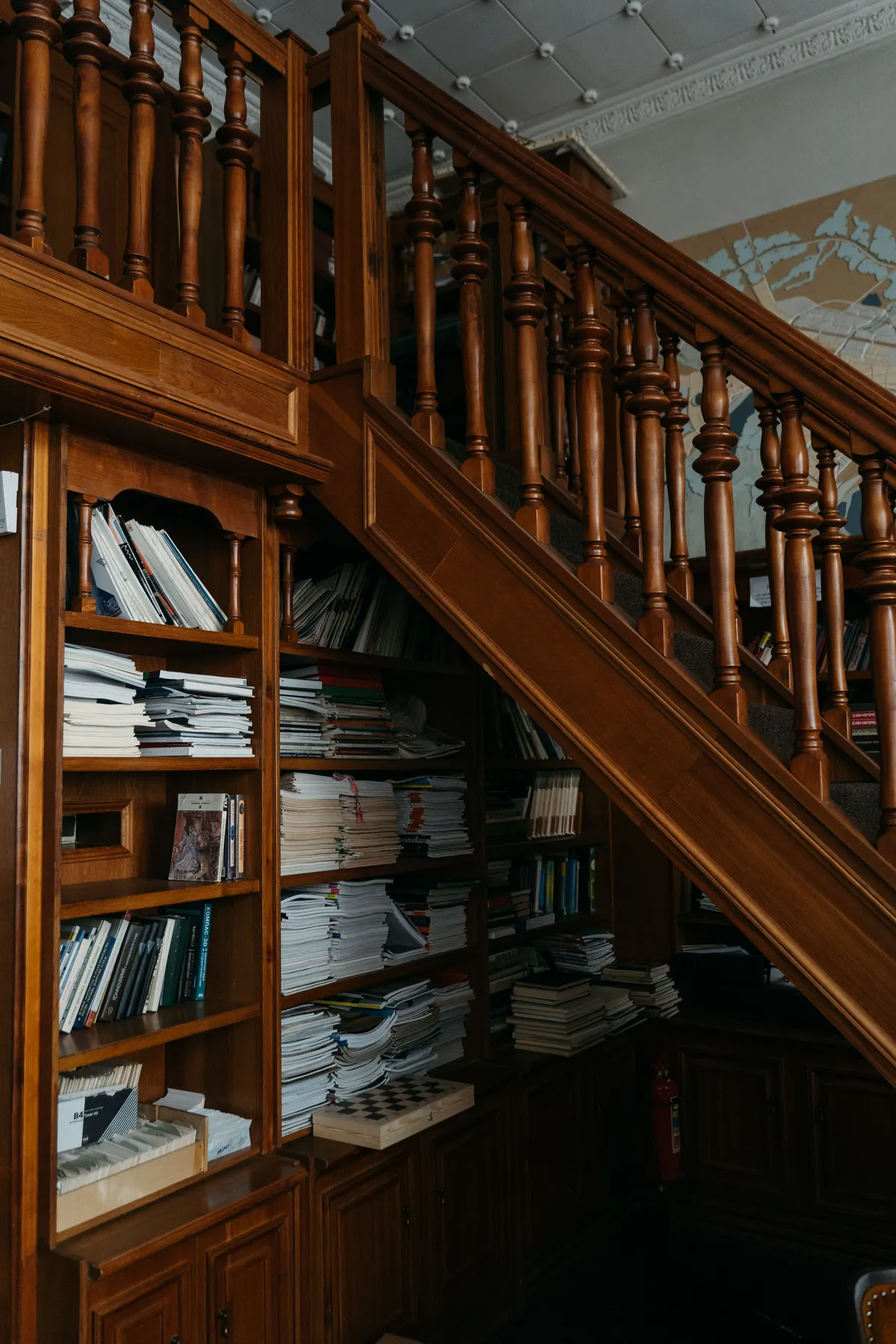 Cozy library corner with wooden bookshelves and staircase, filled with books and papers.