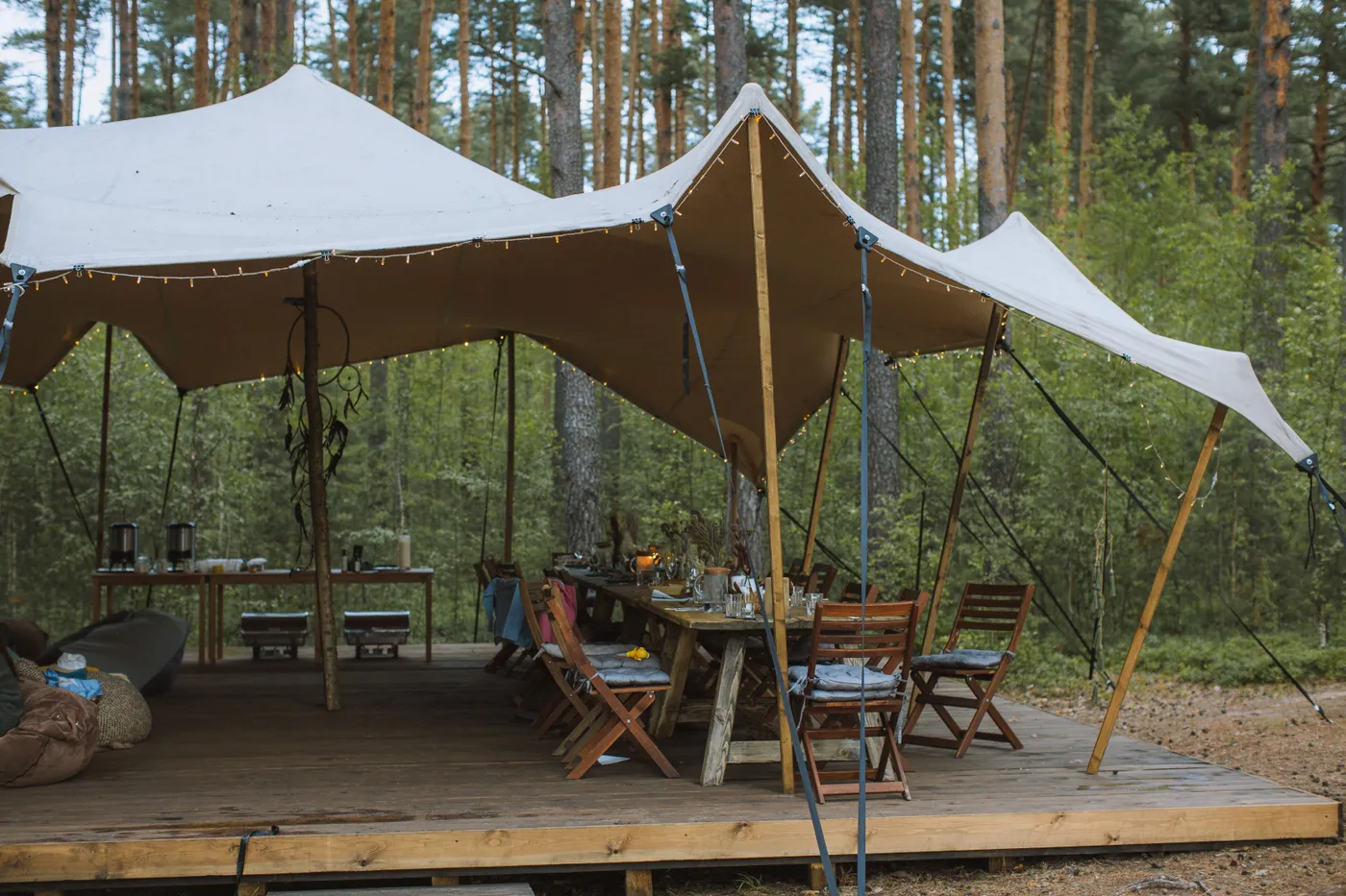 Cozy outdoor campsite with a large tent and wooden tables set in a forest environment, perfect for relaxation.