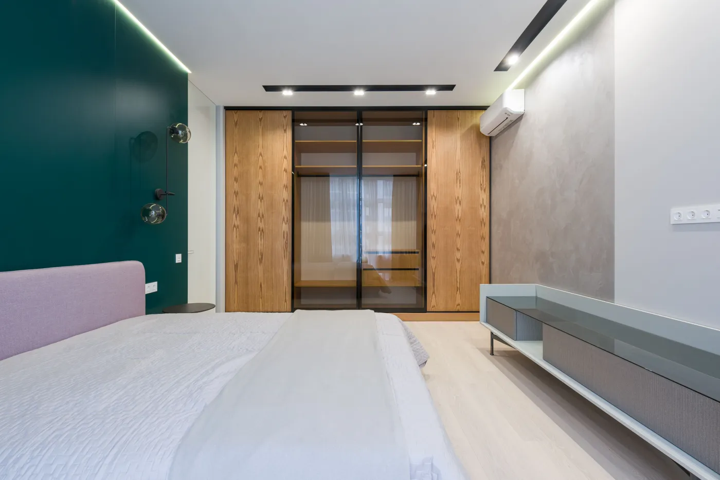 Creative wardrobe with wooden and glass doors in spacious room with comfortable bed in modern apartment