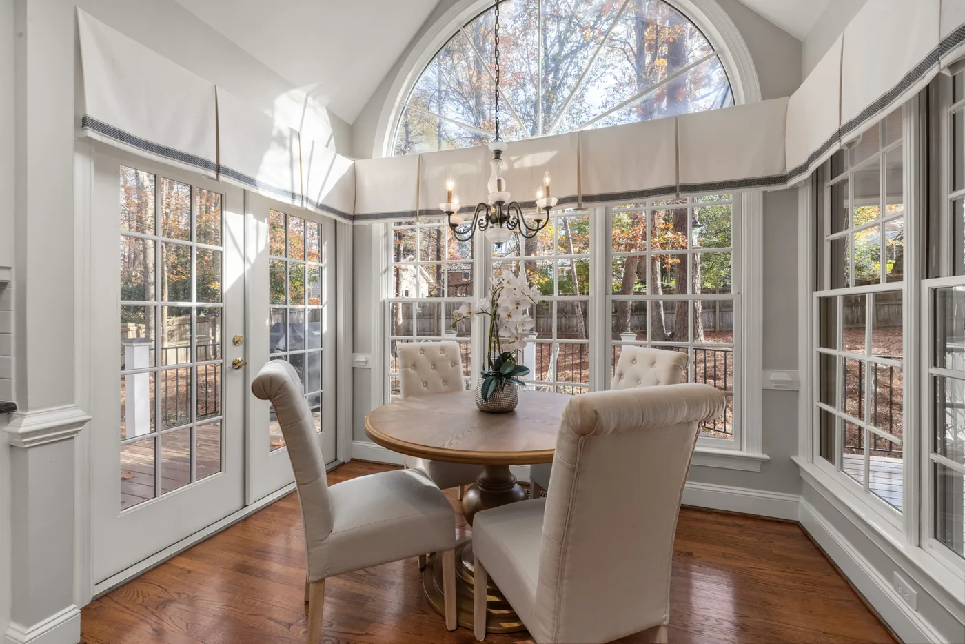 Elegant dining room with a round table, chandelier, and large windows overlooking a garden.